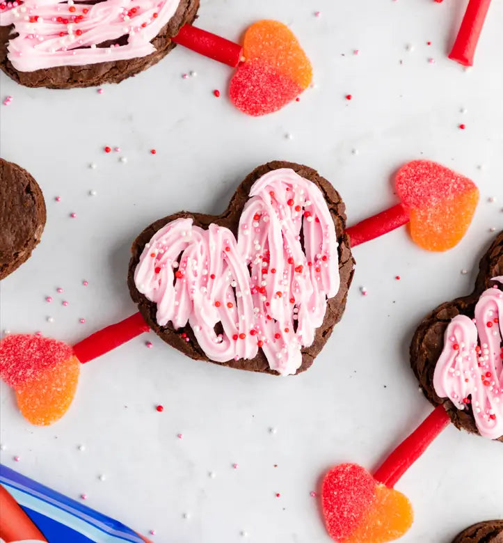 Brownies with pink frosting, sprinkles, and red heart shaped arrows