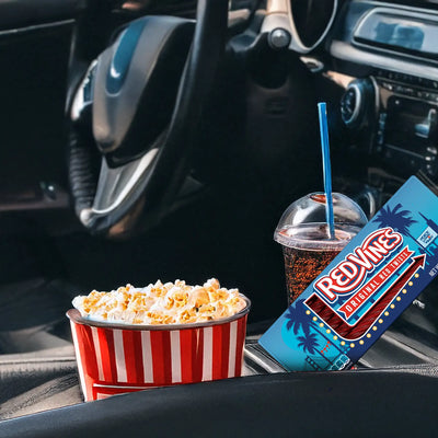 Red Vines Original Twists Tray with a drive in movie theme leaning in a cars cup holder next to a drink and a popcorn bucket