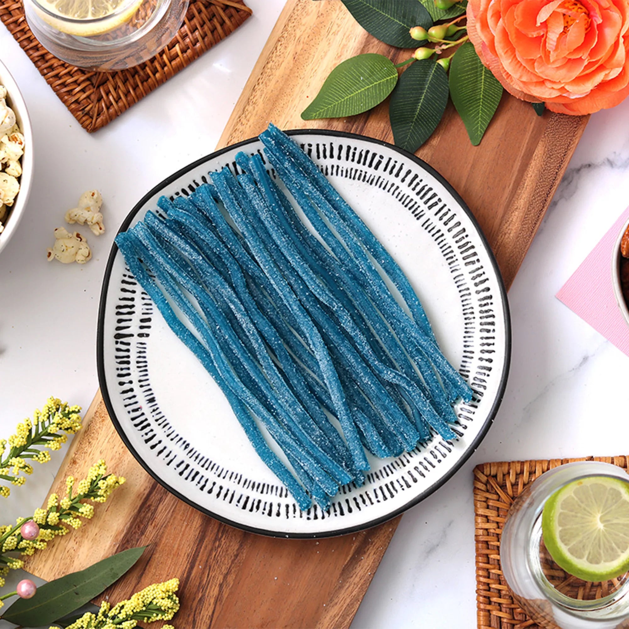 Sour Punch Blue Raspberry Straws candy on a plate surrounded by spring flowers and other snacks