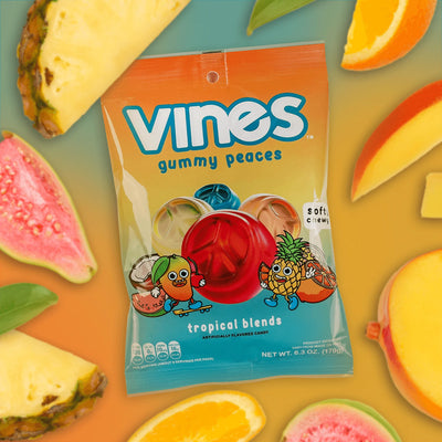 Vines Gummies tropical blends 6.3oz bag on a green to orange gradient background surrounded by tropical fruits