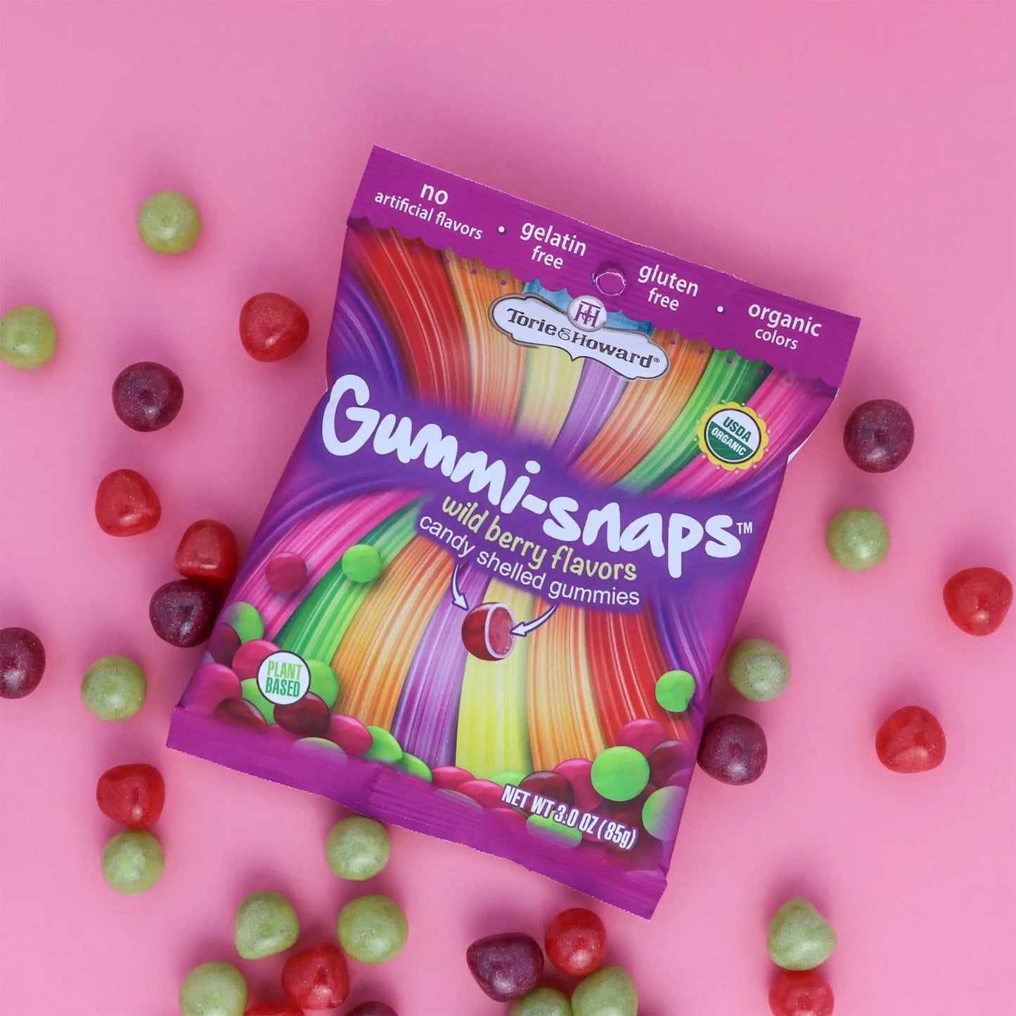Cylindrical shaped red, purple, and green candy scattered around a Torie & Howard Gummi-Snaps Wild Berry Flavors Bag