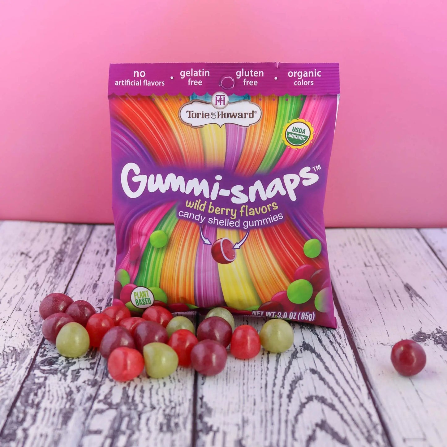 Cylindrical shaped red, purple, and green candy in front of a Torie & Howard Gummi-Snaps Wild Berry Flavors Bag