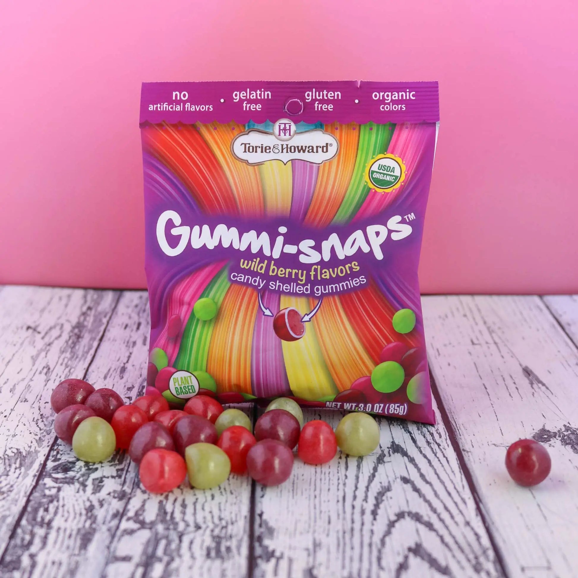 Cylindrical shaped red, purple, and green candy in front of a Torie & Howard Gummi-Snaps Wild Berry Flavors Bag