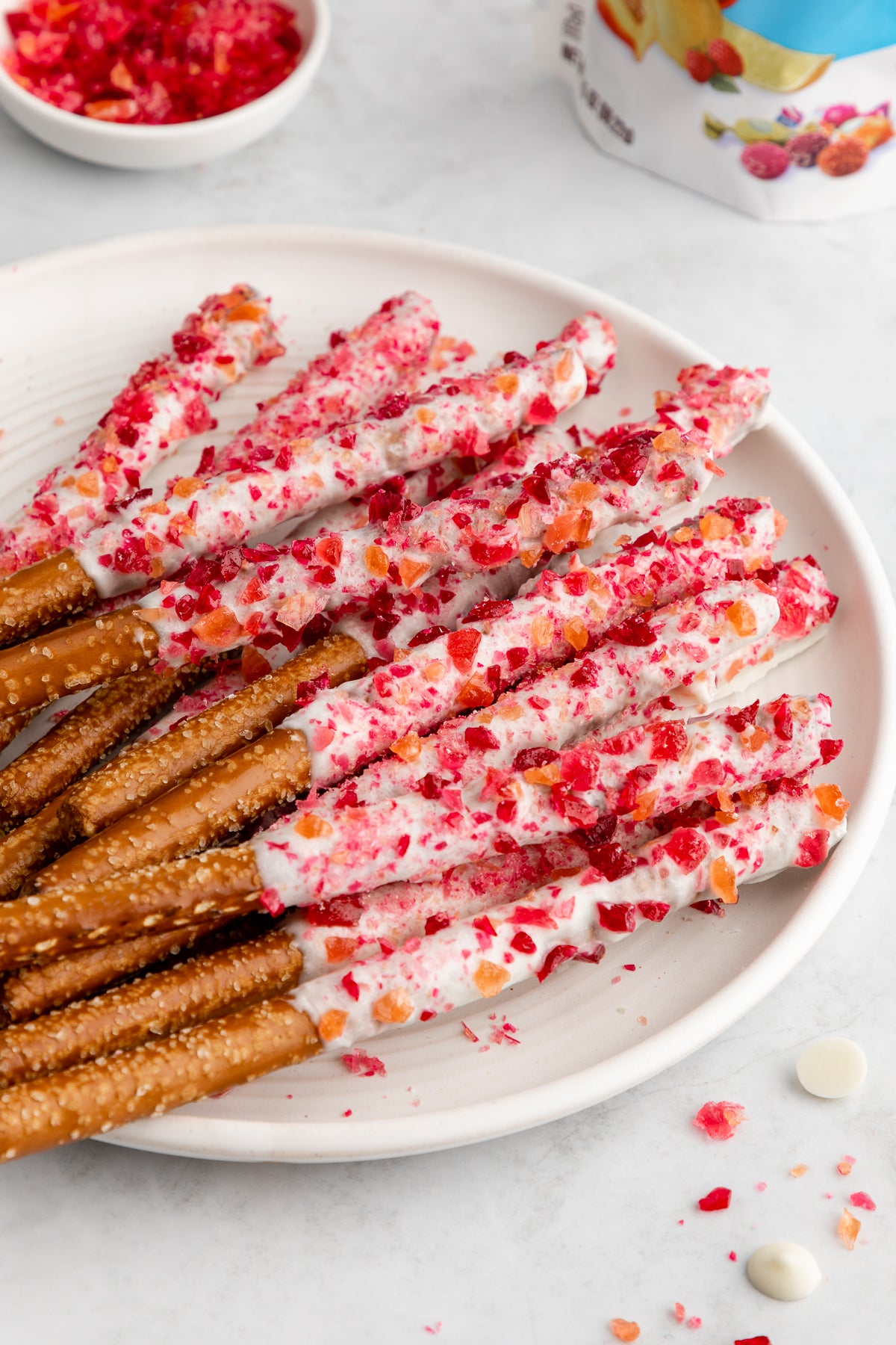 White Chocolate Covered Pretzel Rods on a plate next to a bag of Assorted Organic Hard Candy