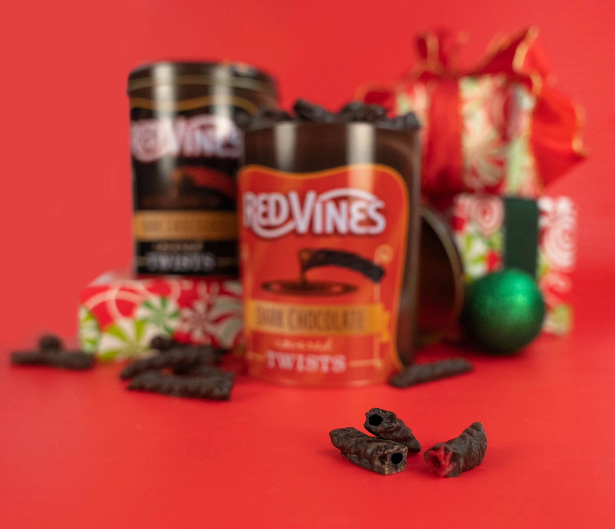 Red Vines Chocolate Covered Twists surrounded by holiday gifts and decor, with raw chocolate-enrobed candy pieces in the forefront