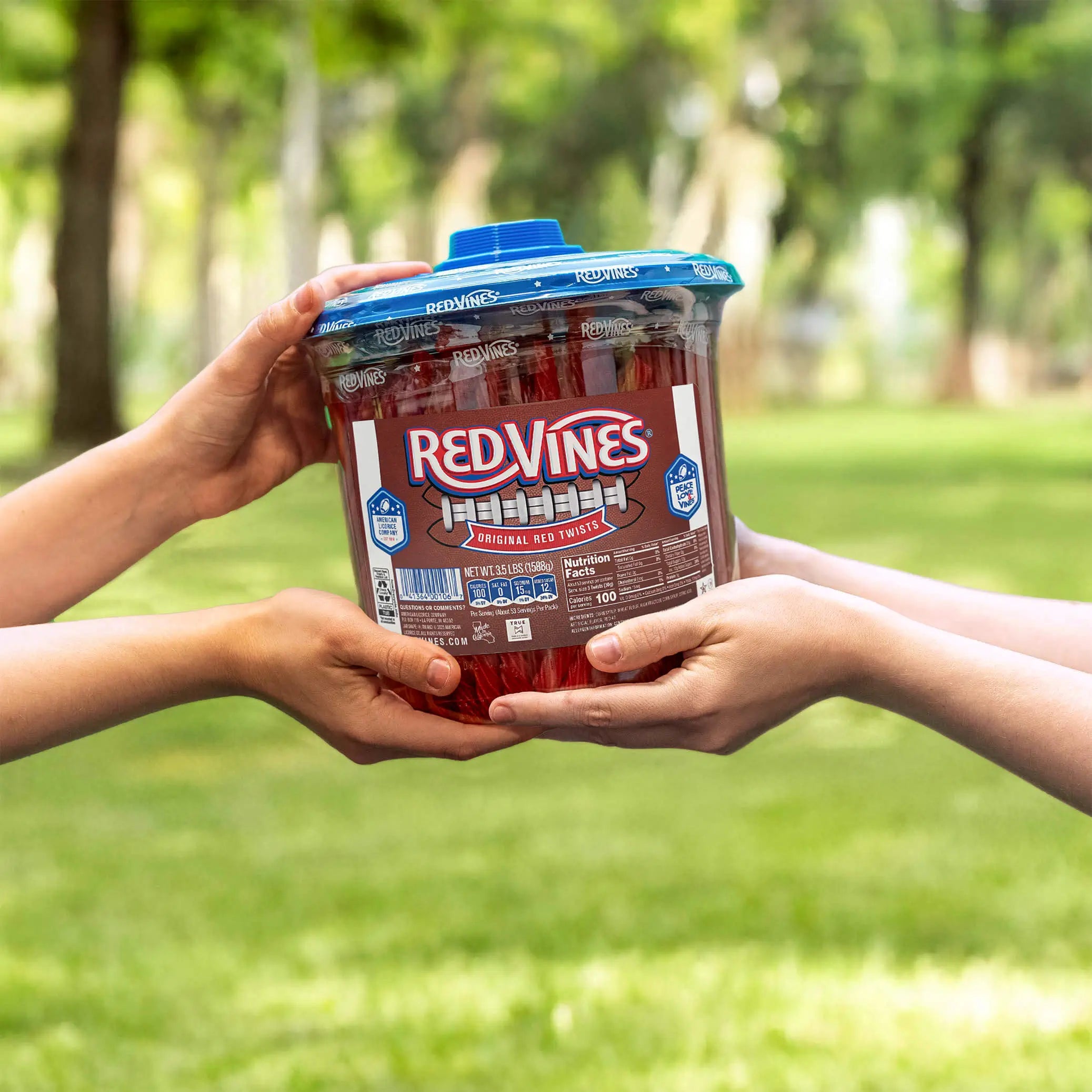 Two people passing a Red Vines Original Red Licorice Candy Twists 3.5lb Jar in limited-edition football graphics