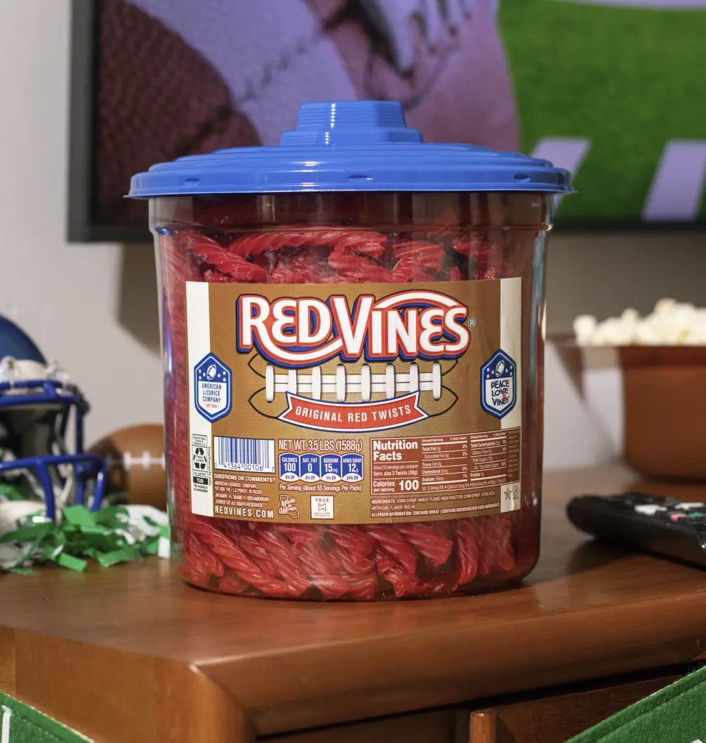 Front of Red Vines Original Red Licorice Twists 3.5lb Jar in limited-edition football graphics, sitting on a coffee table while the big game is on TV