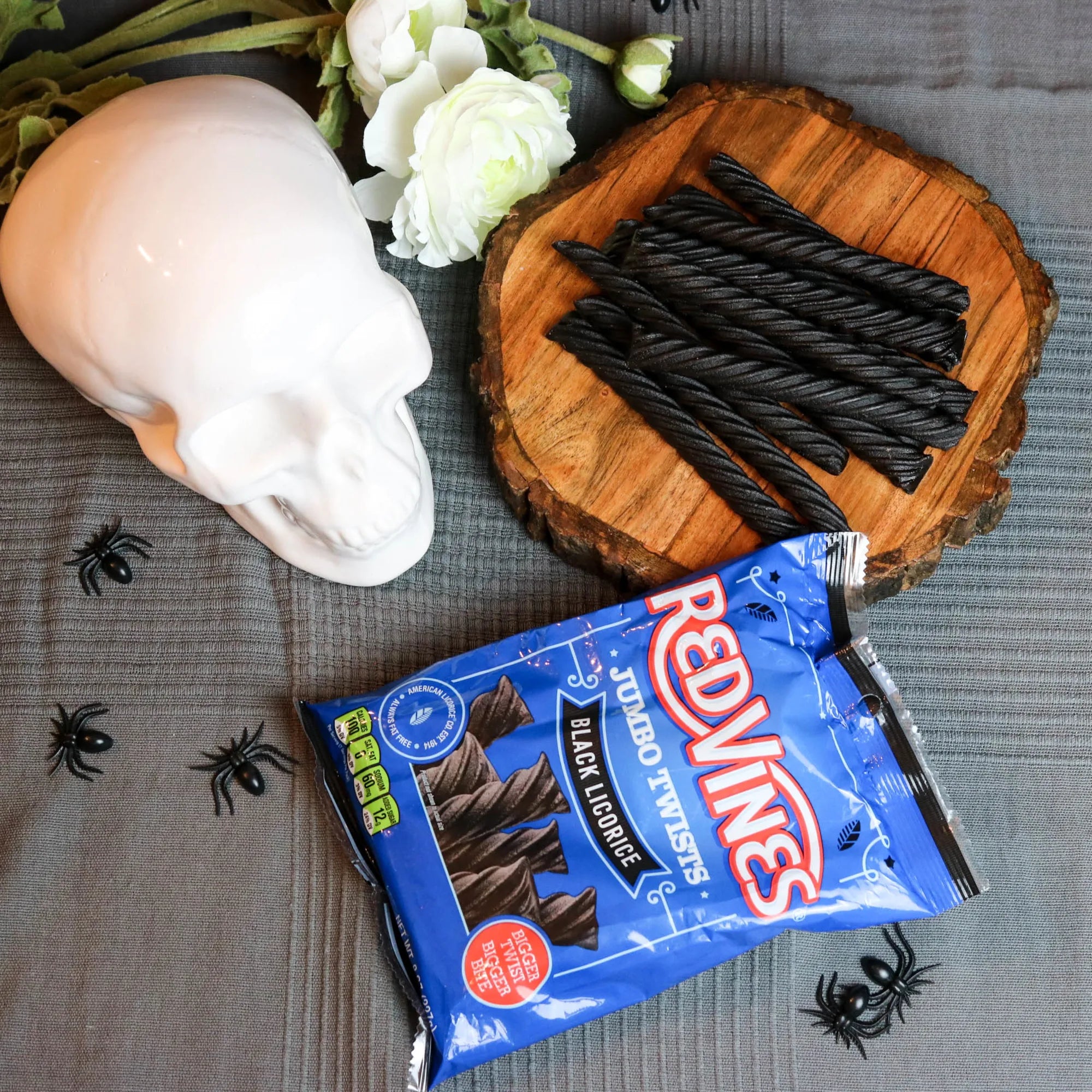 Red Vines Jumbo Black Licorice Candy in a spooky Halloween scene with fake spiders, a white skull and white roses