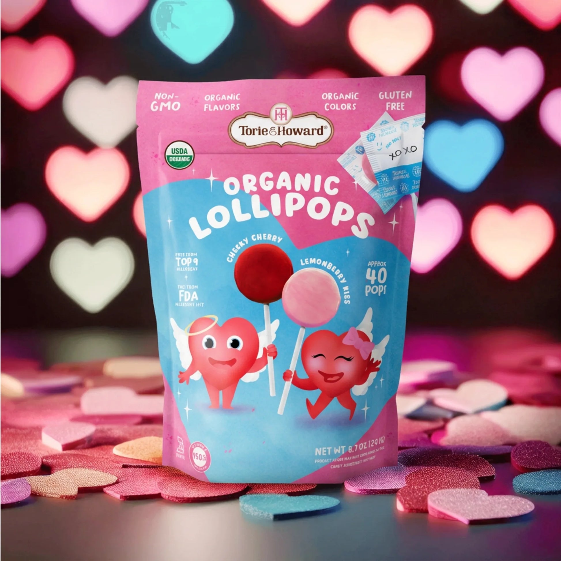 Torie & Howard Organic Valentine's Candy Lollipops on black table with multi-colored heart lights in background 