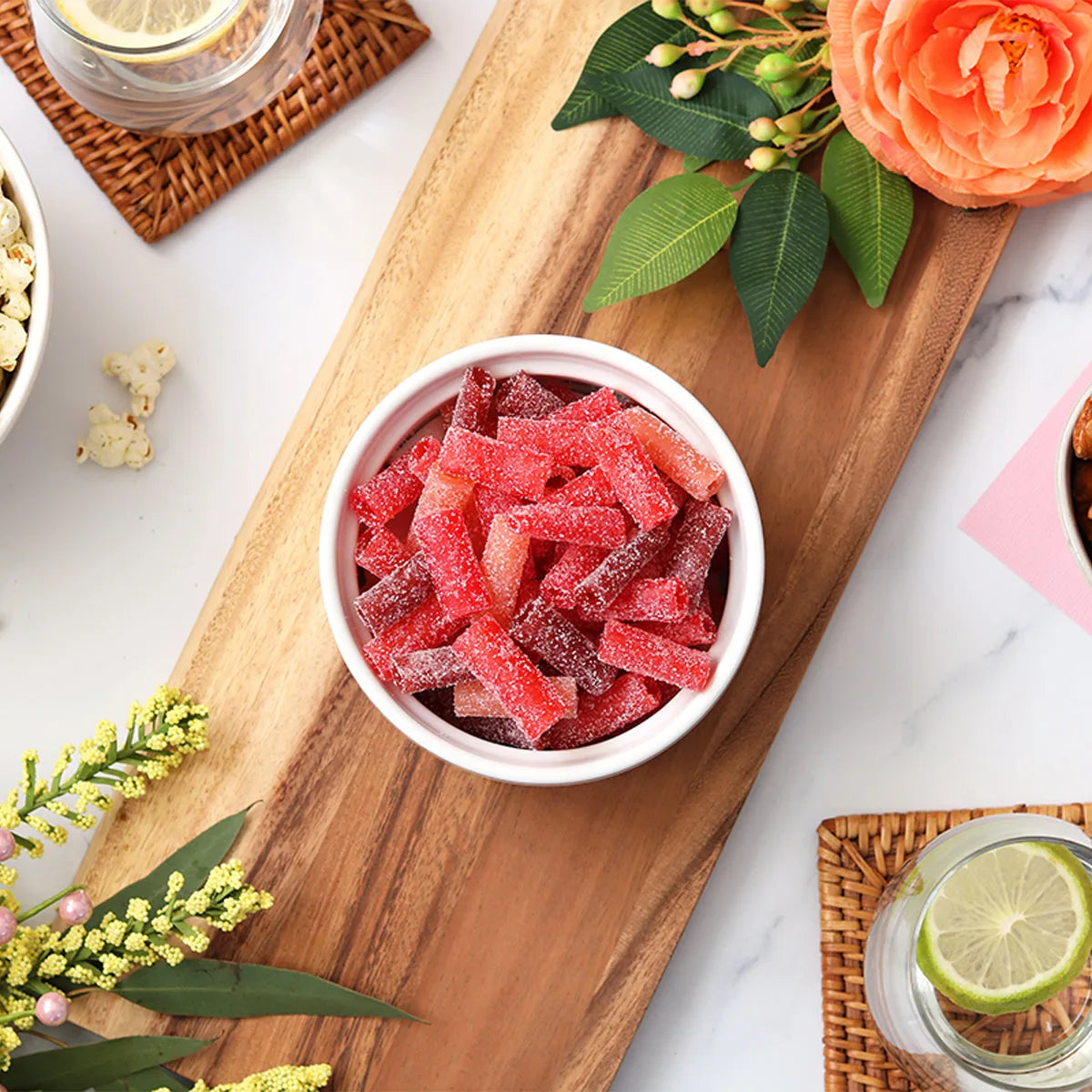 Sour Punch Rad Reds Bites candy in a dish surrounded by spring flowers and other snacks