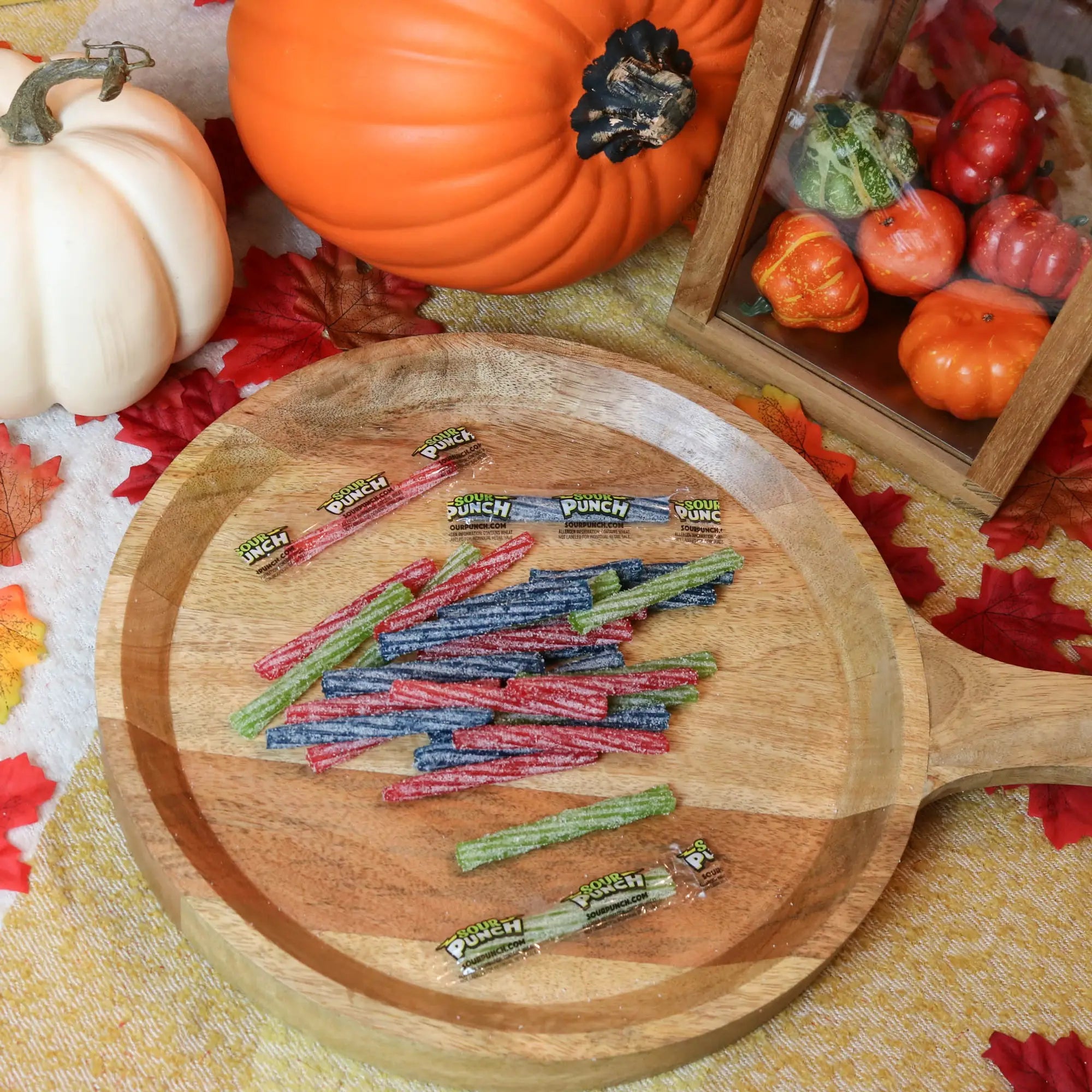 Sour Punch Individually Wrapped 3in Twists Assorted Candy on a round wooden plate surrounded by pumpkins and leaves