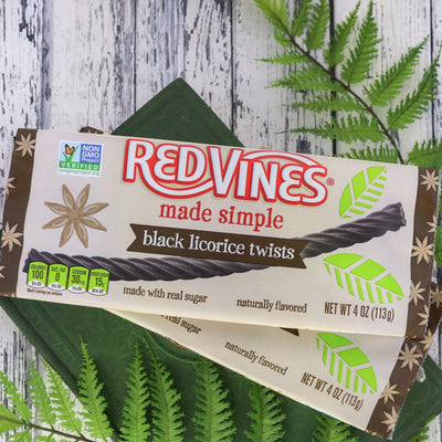 Two RED VINES Made Simple Black Licorice Twists 4oz Trays on natural wood and evergreen branches