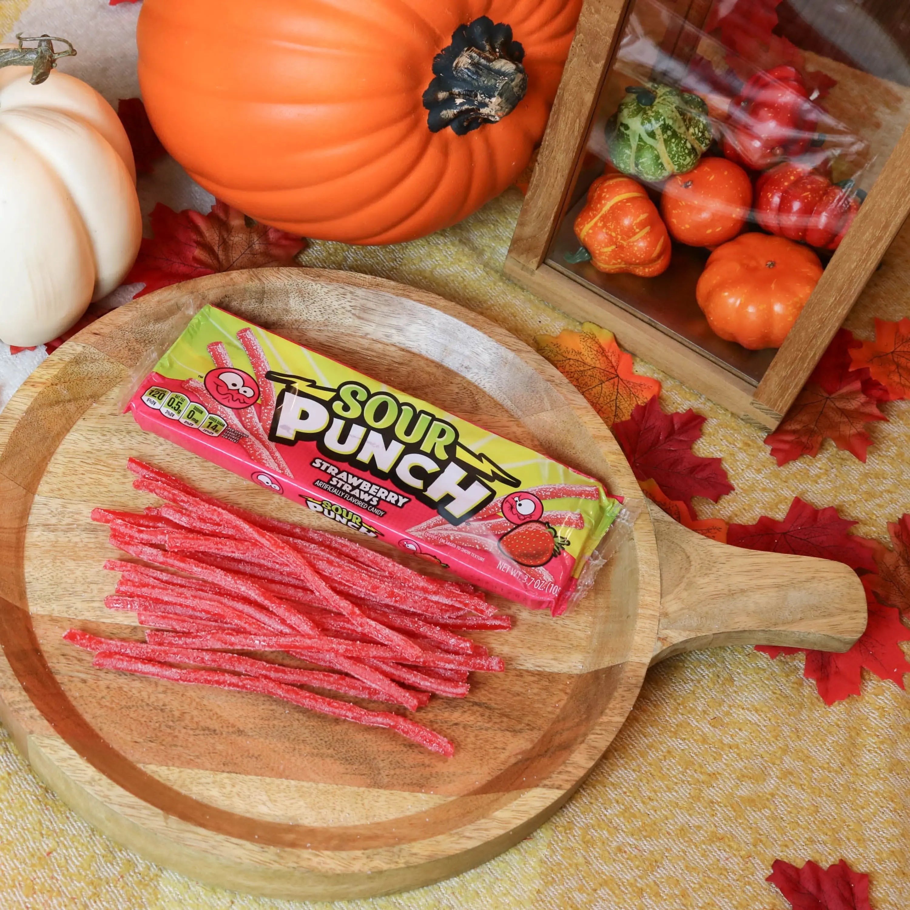 Sour Punch Strawberry Straws Candy on a round wooden plate surrounded by pumpkins and leaves