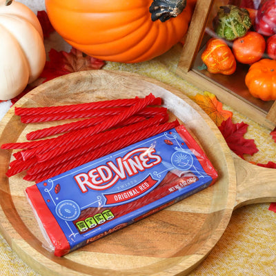 Red Vines Original Red Licorice Candy 5oz tray on a round wooden plate surrounded by pumpkins and leaves