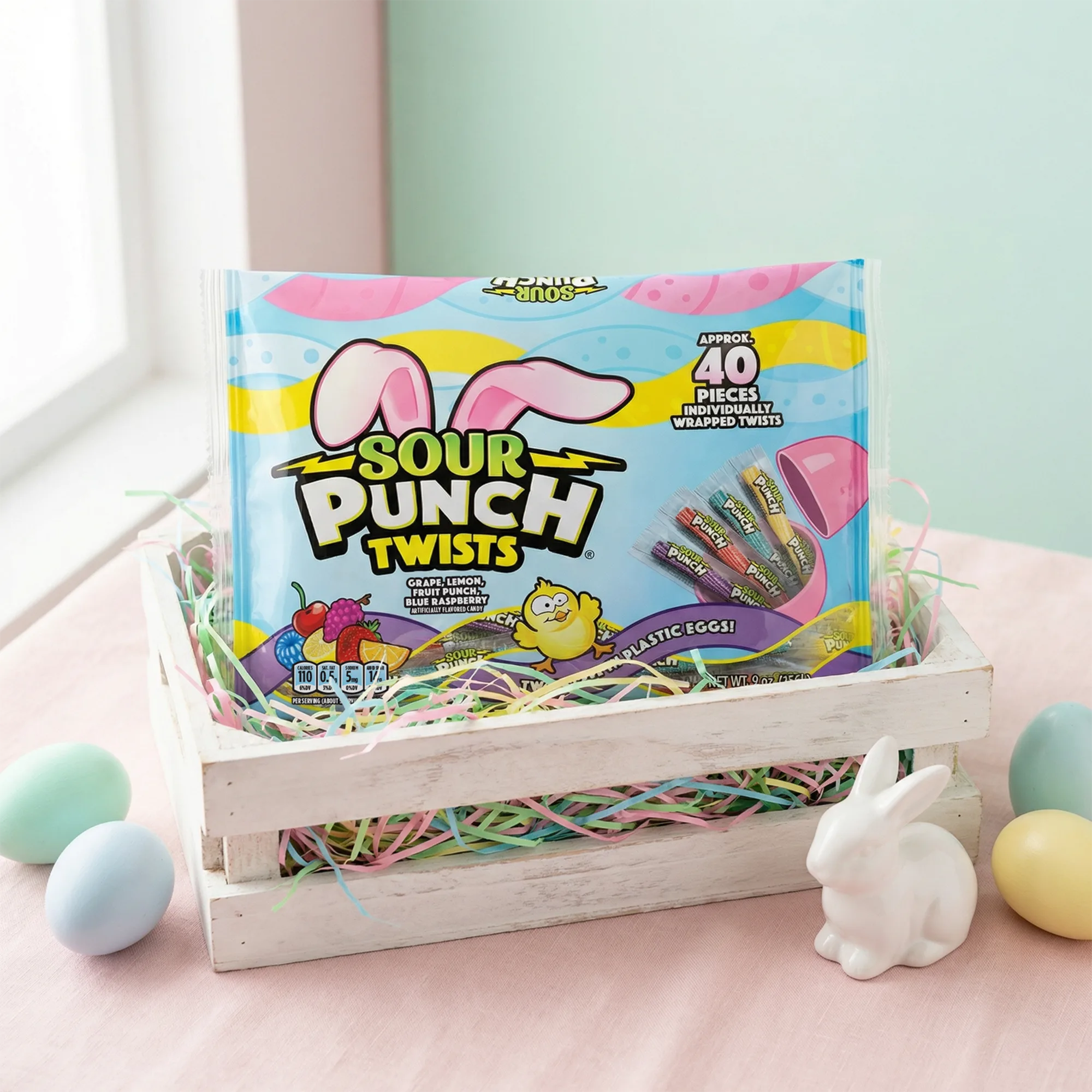 Sour Punch Easter Twists in a white wooden crate with confetti, surrounded by dyed eggs and a white bunny figurine