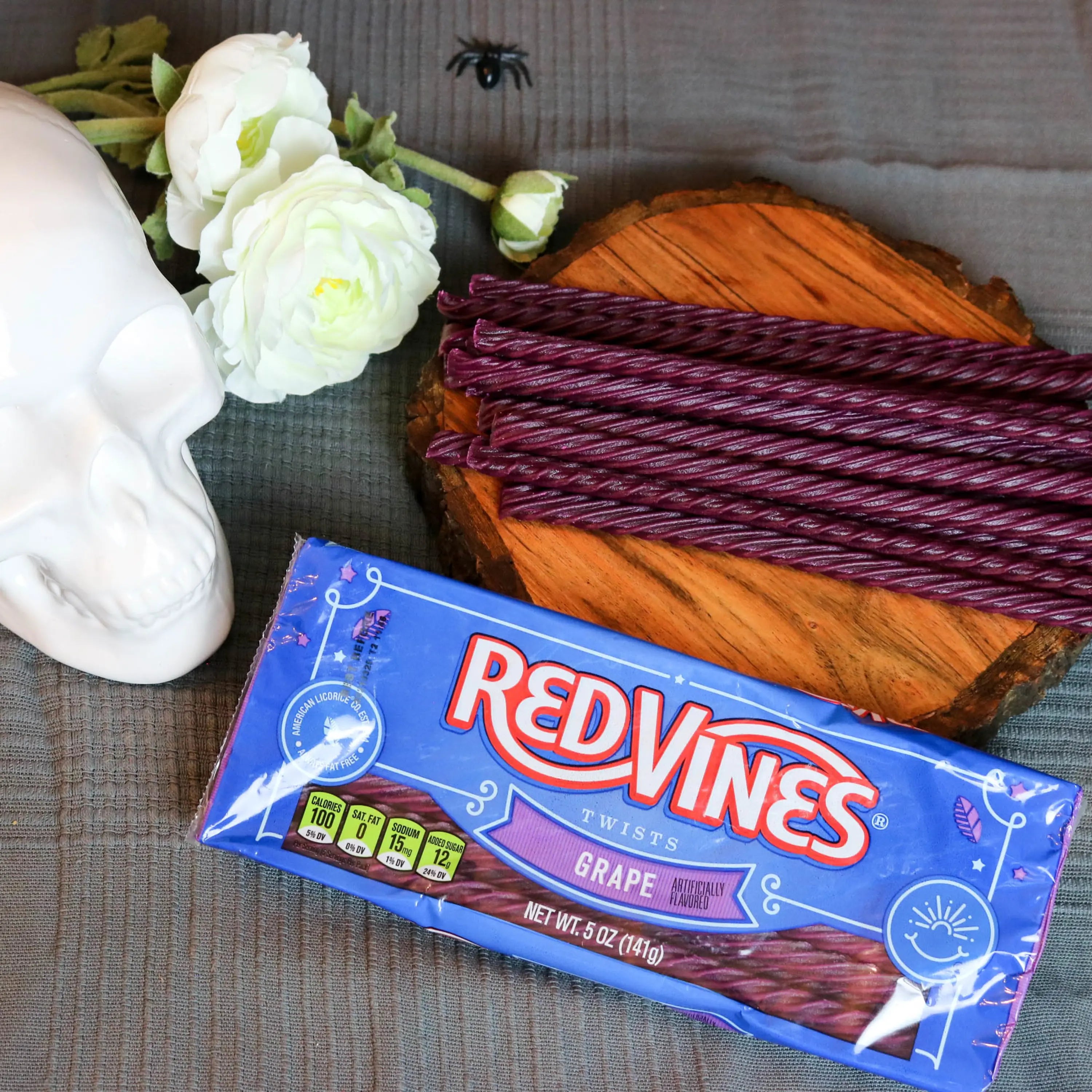 Red Vines Grape Licorice Candy in a spooky Halloween scene with fake spiders, a white skull and white roses