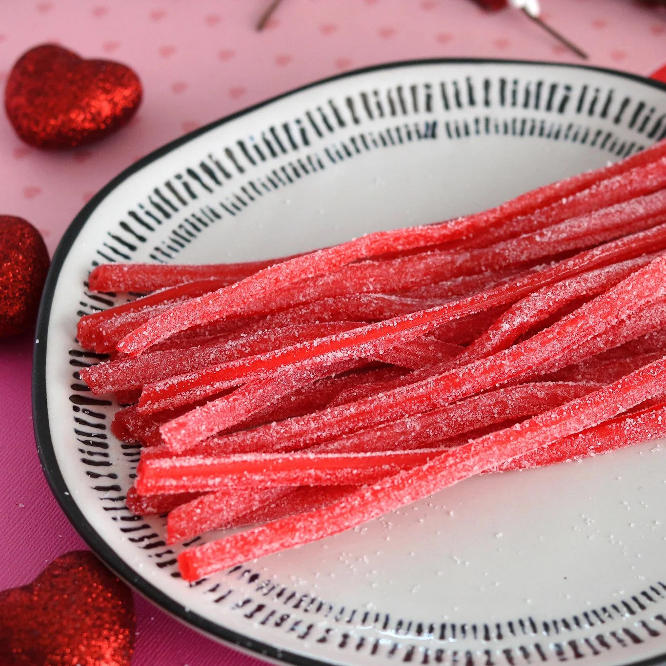 SOUR PUNCH Strawberry Straws candy on a white plate surrounded by red sparkle hearts