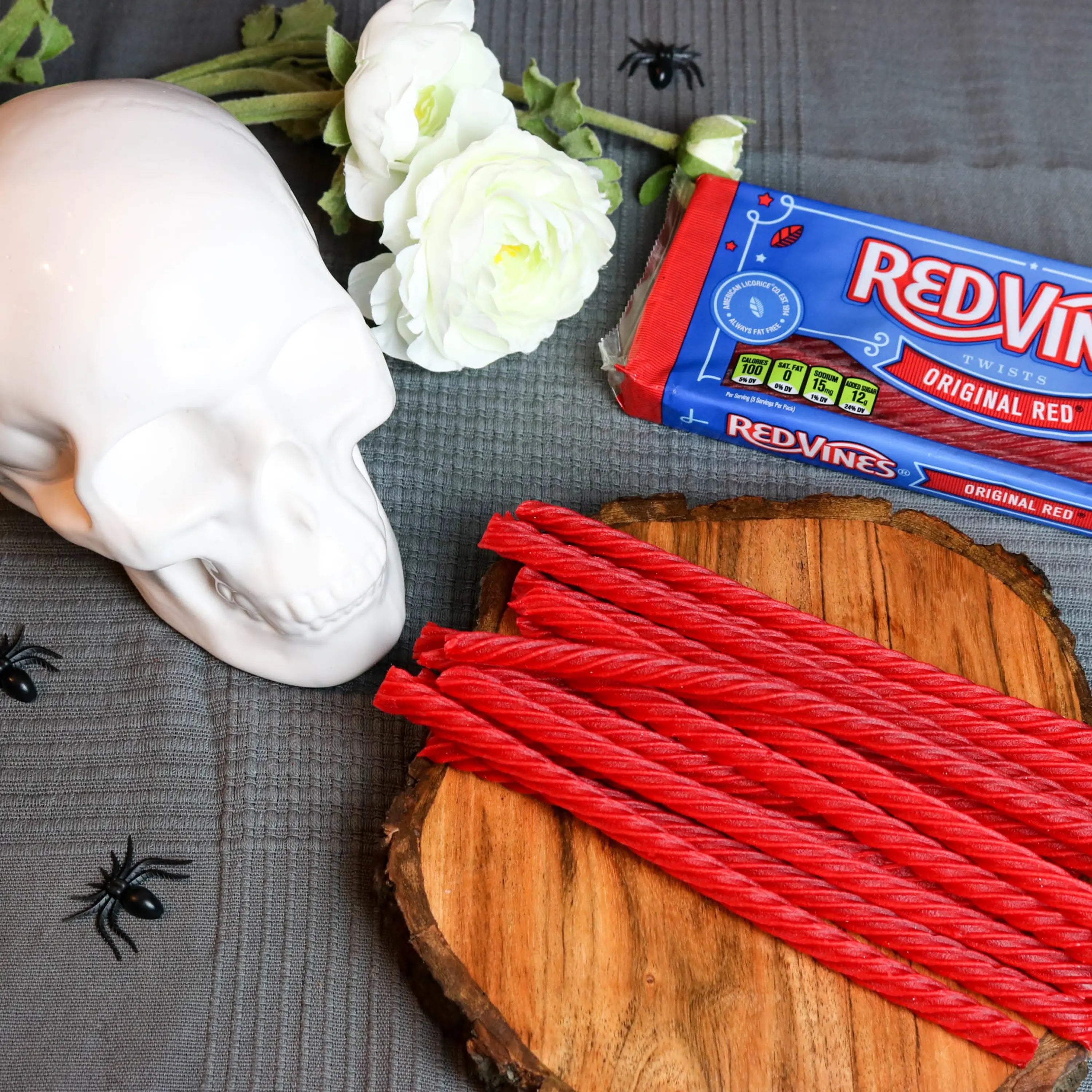 Red Vines Original Red Licorice Candy 5oz tray in a spooky Halloween scene with fake spiders, a white skull and white roses