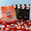 Red Vines Original Red Minis Bag next to a film clapper board, surrounded by mini red licorice pieces and popcorn