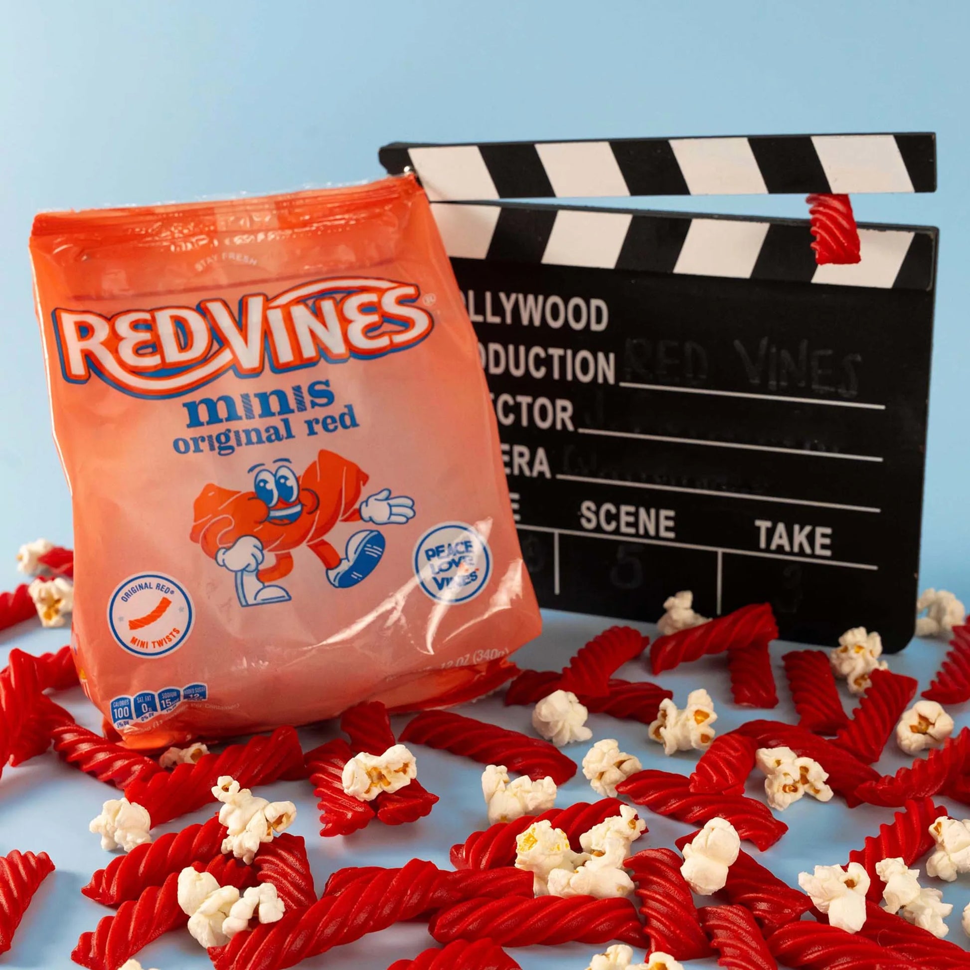 Red Vines Original Red Minis Bag next to a film clapper board, surrounded by mini red licorice pieces and popcorn