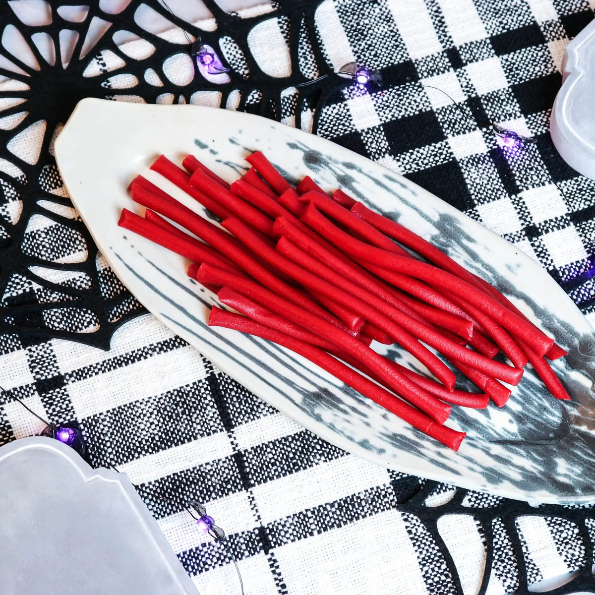 Red Ropes Licorice Rope Candy on a gray serving tray on a platter with a fake spiderweb and tombstone