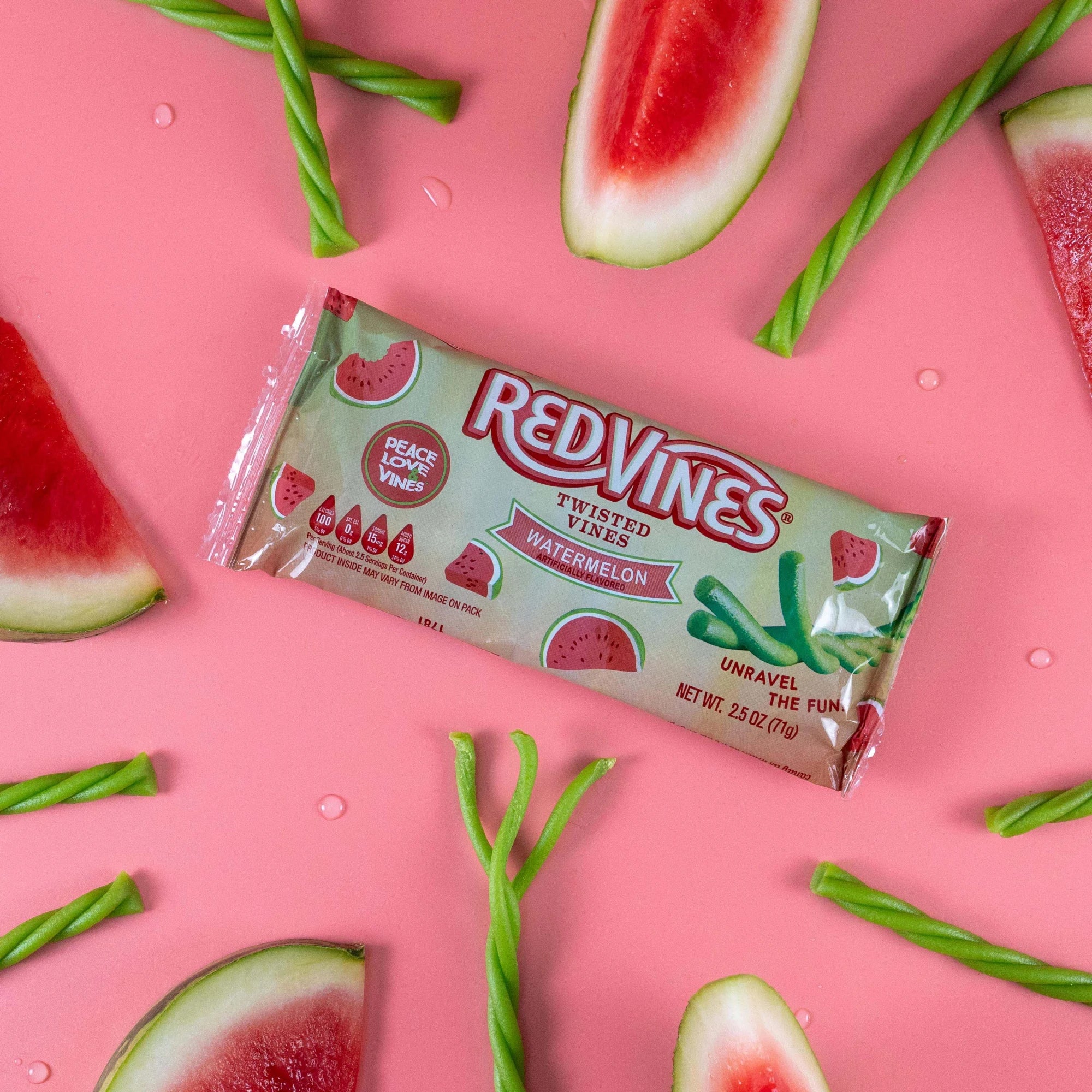 Red Vines Watermelon Twisted Vines 2.5oz Bag on a pink background with raw watermelon candy pieces and real watermelon quarters