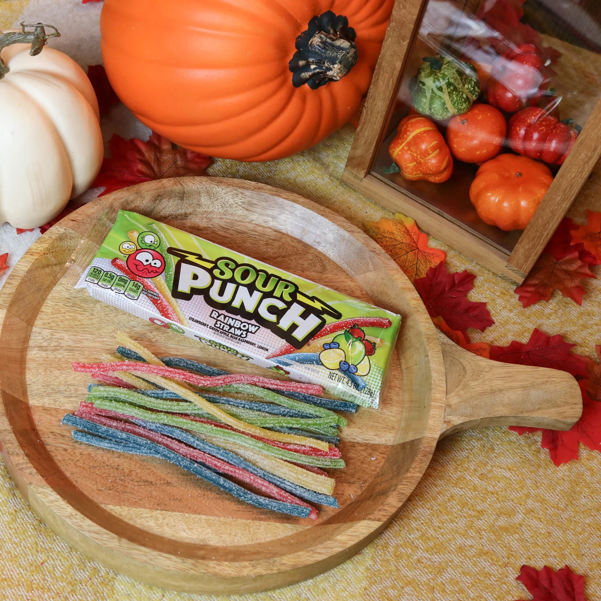 Sour Punch Rainbow Straws Candy on a round wooden plate surrounded by pumpkins and leaves