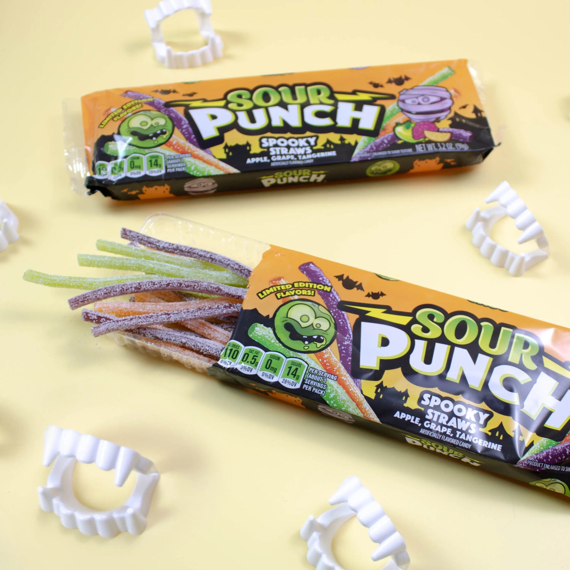 Two trays of SOUR PUNCH Spooky Straws Halloween Candy alongside plastic fangs for Halloween