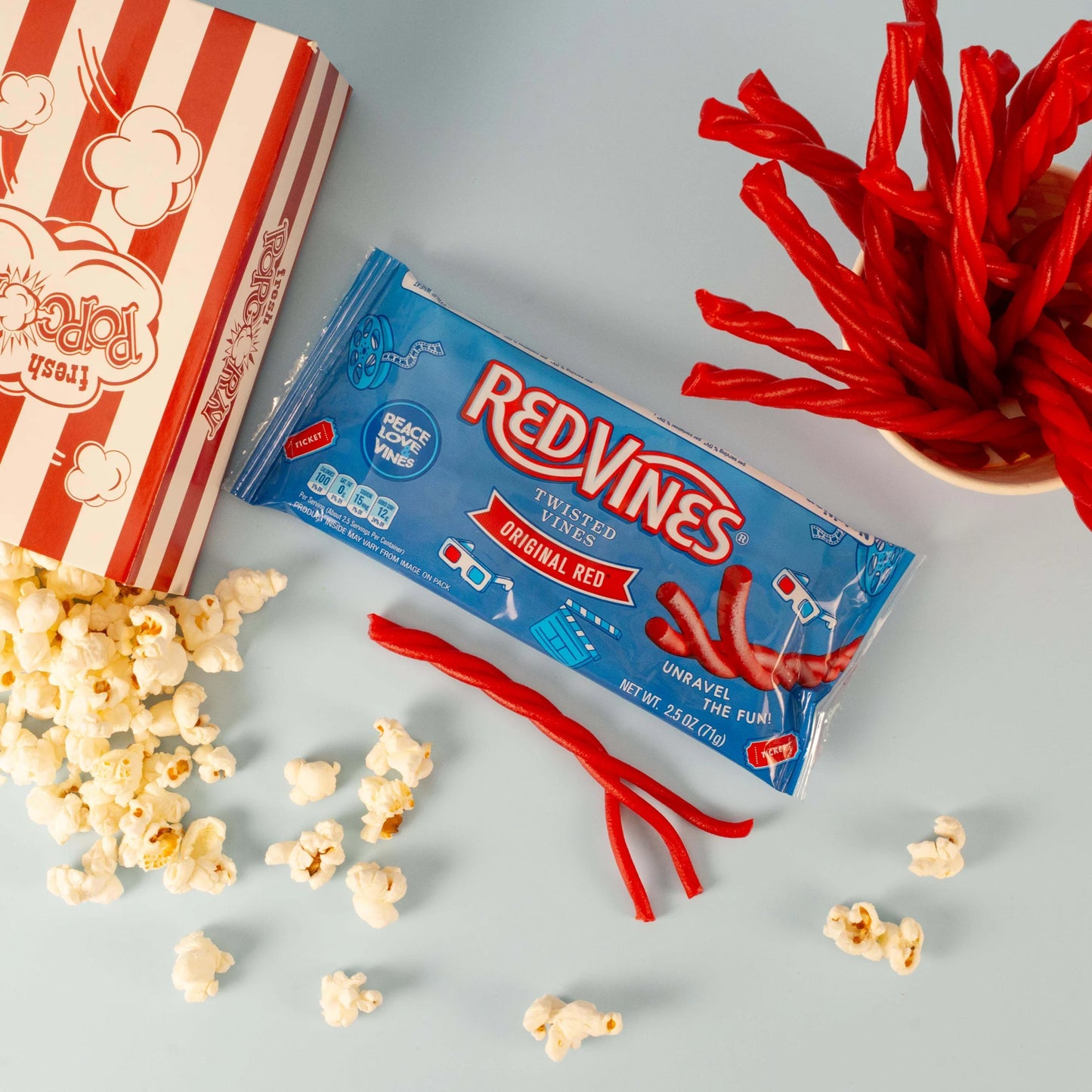 Red Vines Original Red Twisted Vines 2.5oz Bag with a tub of popcorn and raw peelable licorice pieces