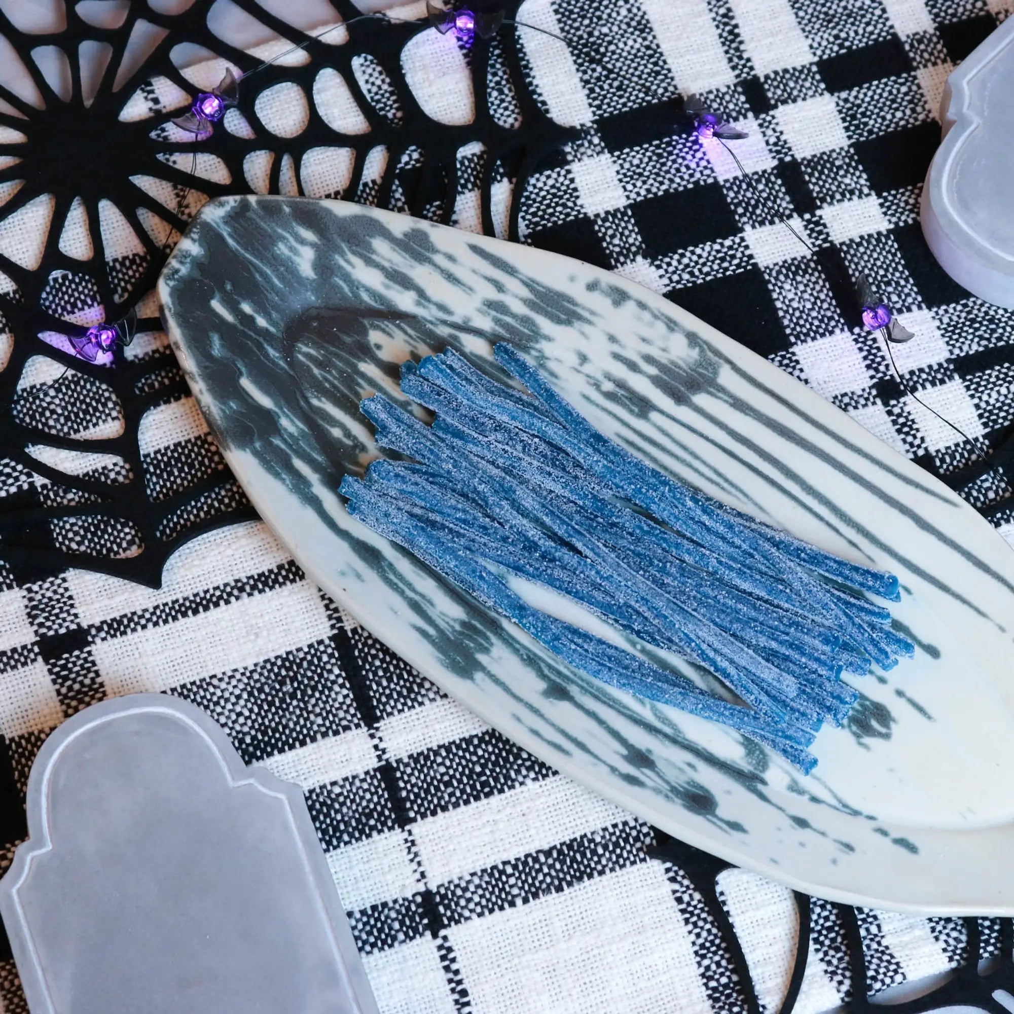 Sour Punch Blue Raspberry Straws Candy on a platter with a fake spiderweb and tombstone