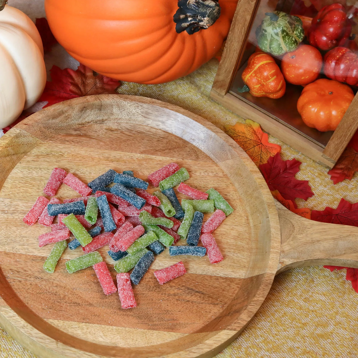 Sour Punch Assorted Bites Candy on a round wooden plate surrounded by pumpkins and leaves
