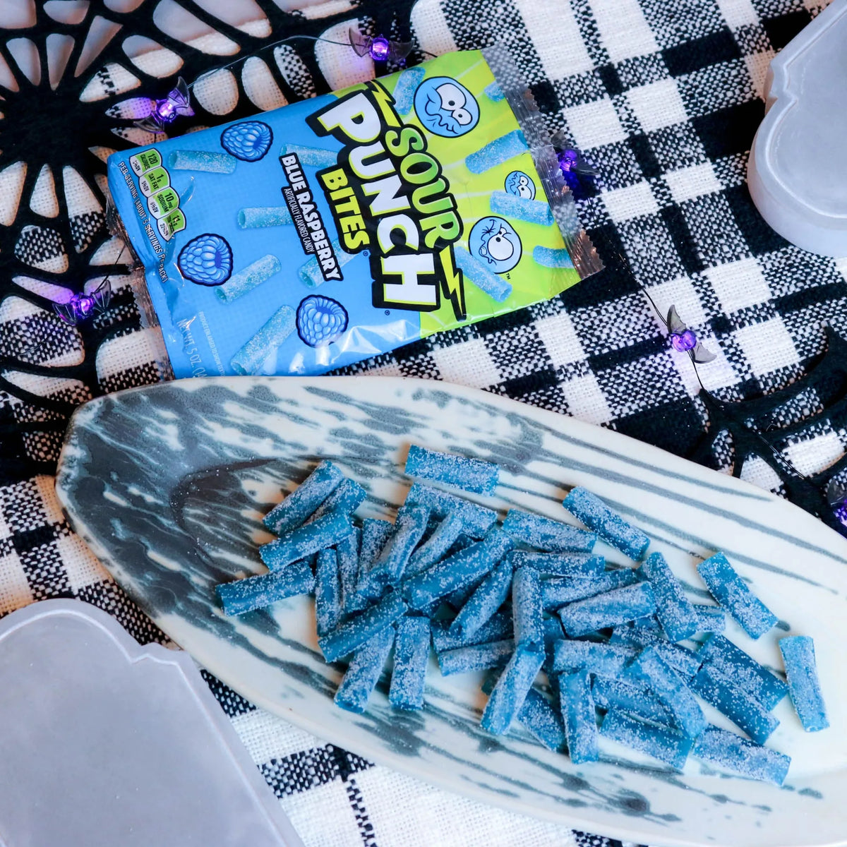 Sour Punch Blue Raspberry Bites Candy on a platter with a fake spiderweb and tombstone