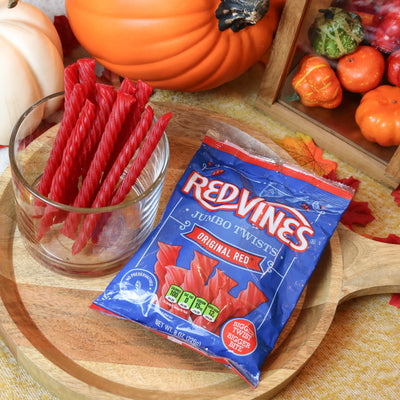 Red Vines Original Red Jumbo Licorice Twists on a wooden platter surrounded by pumpkins and leaves