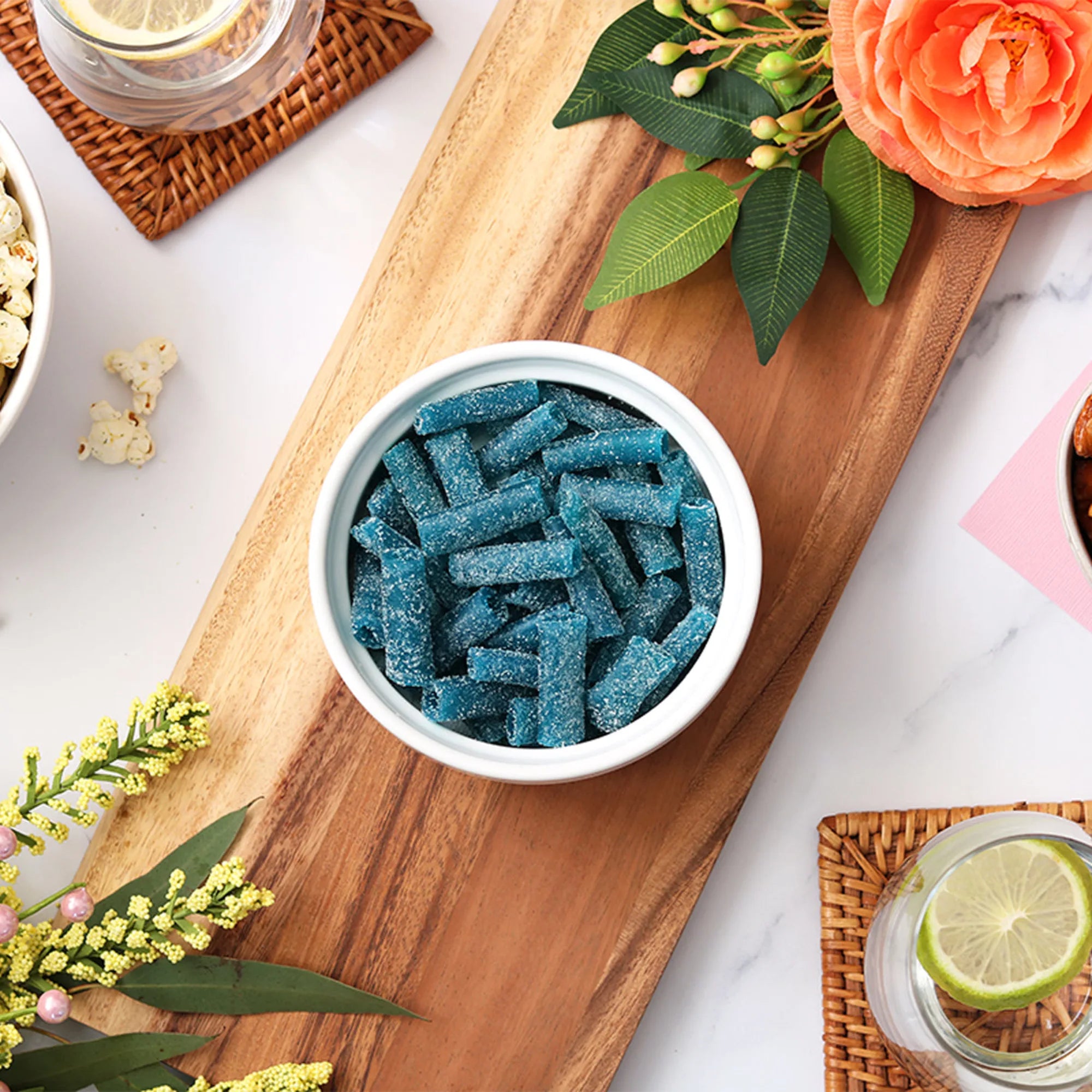 Sour Punch Blue Raspberry Bites candy in a dish surrounded by spring flowers and other snacks