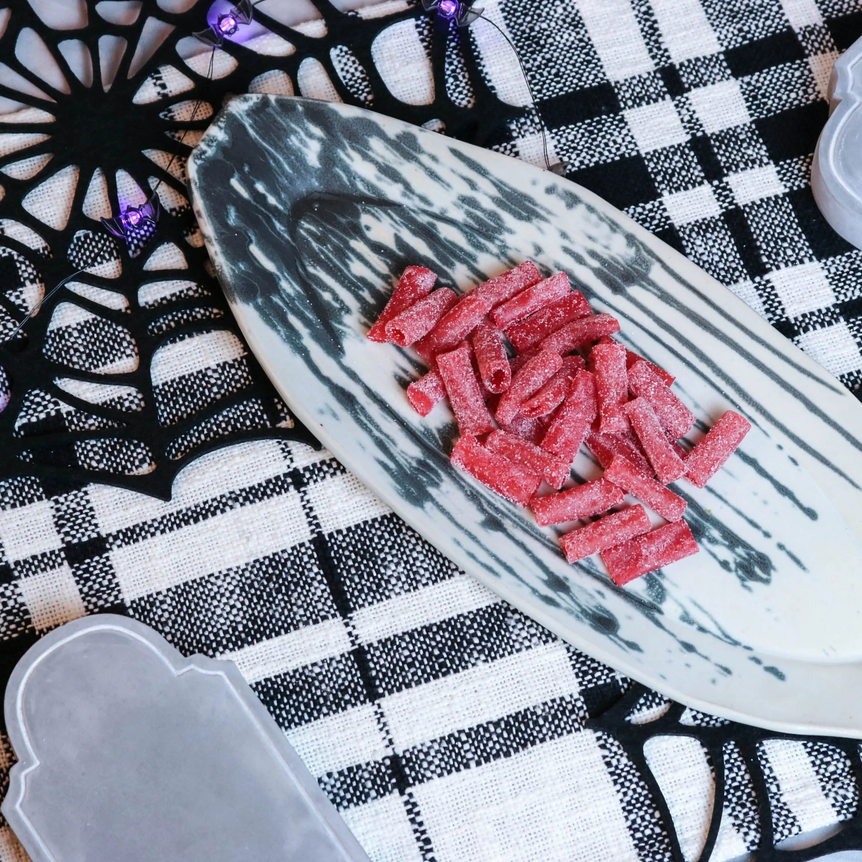 Sour Punch Strawberry Bites Candy on a platter with a fake spiderweb and tombstone