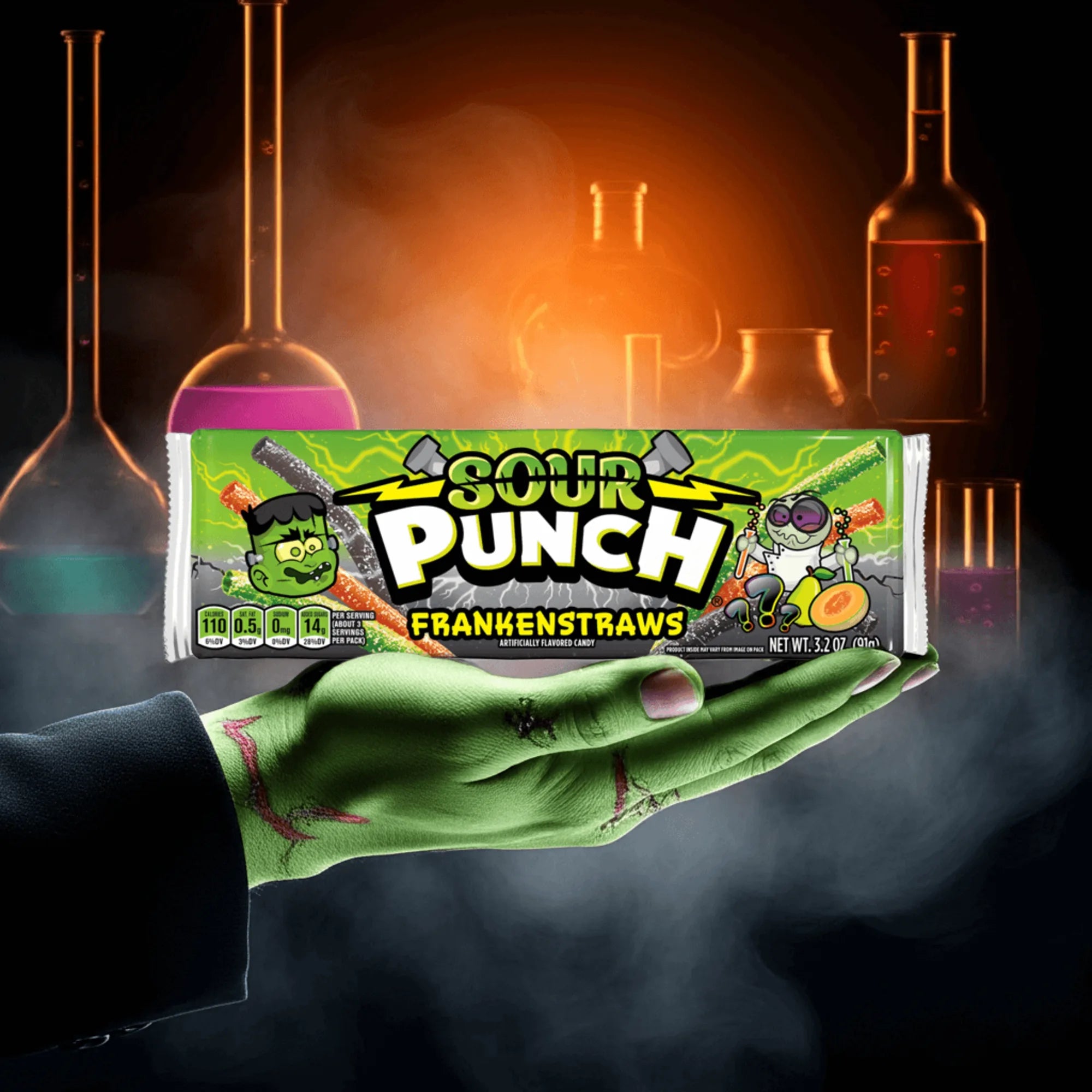 A monsters hand holding a tray of Sour Punch Frankenstraws Halloween Candy in a fog with glowing science beakers behind it
