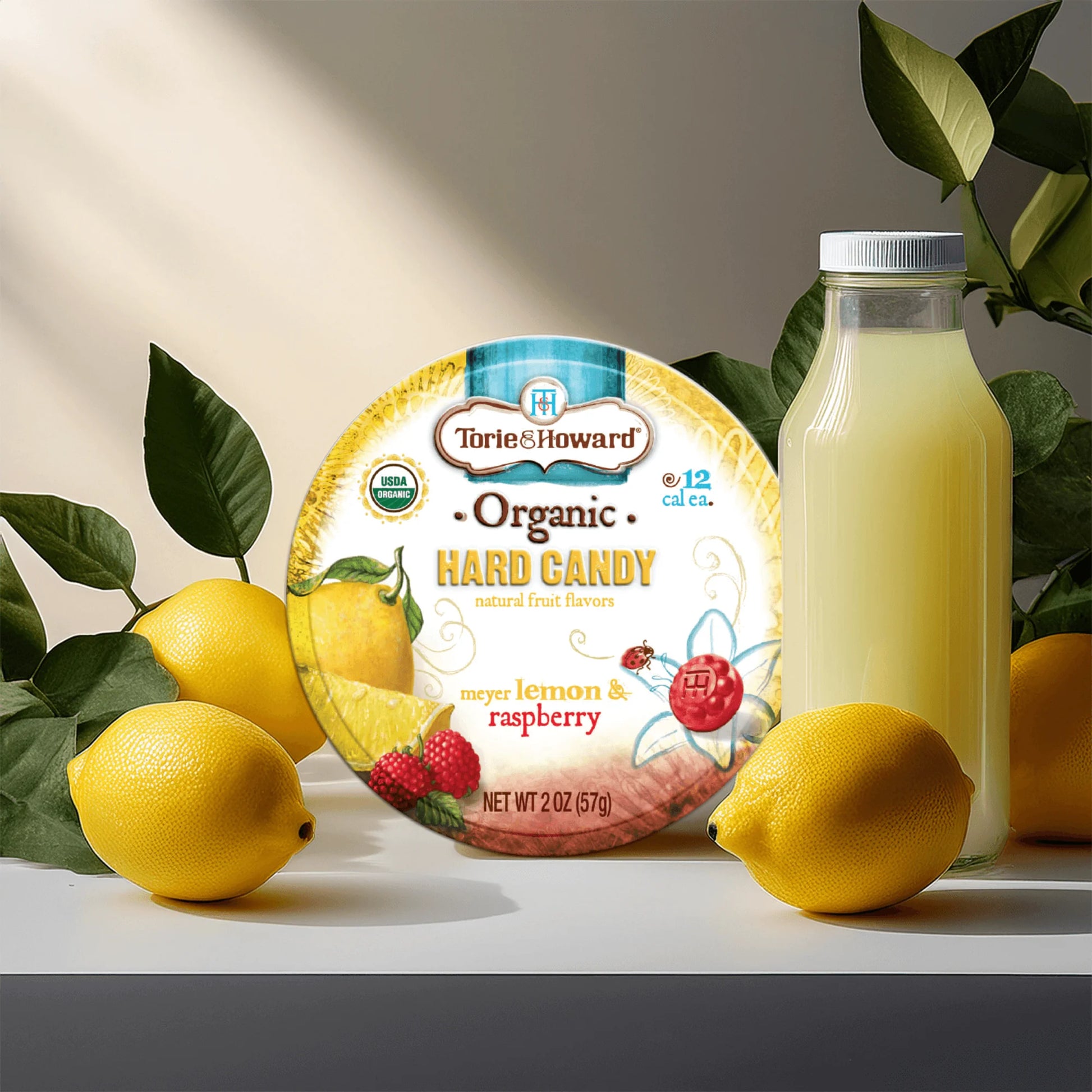 Torie & Howard Meyer Lemon & Raspberry Organic Hard Candy 2oz Tin with lemons and a glass bottle of lemonade