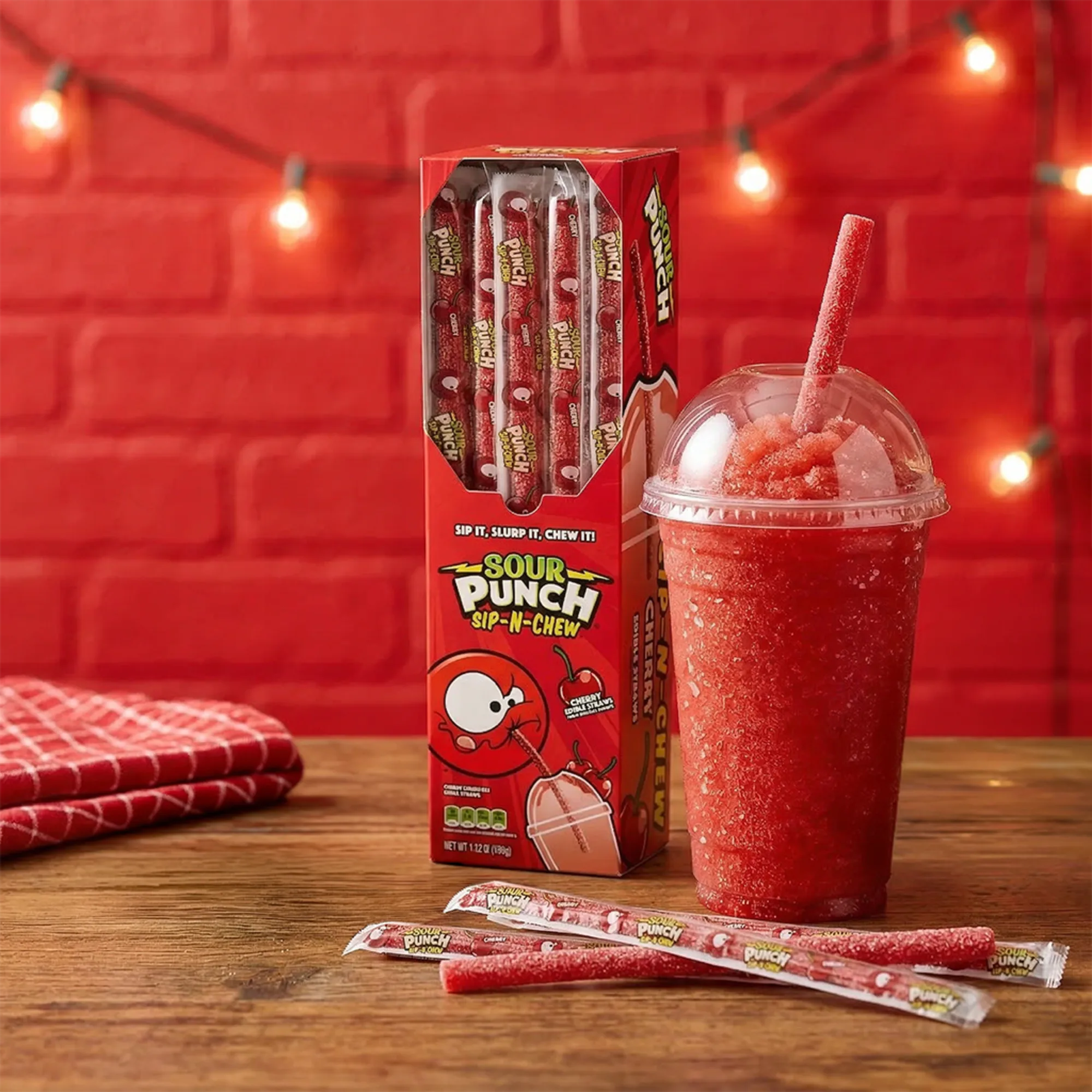 Sour Punch Sip-N-Chew Cherry Straws with a red drink on a wooden surface against a red brick wall.