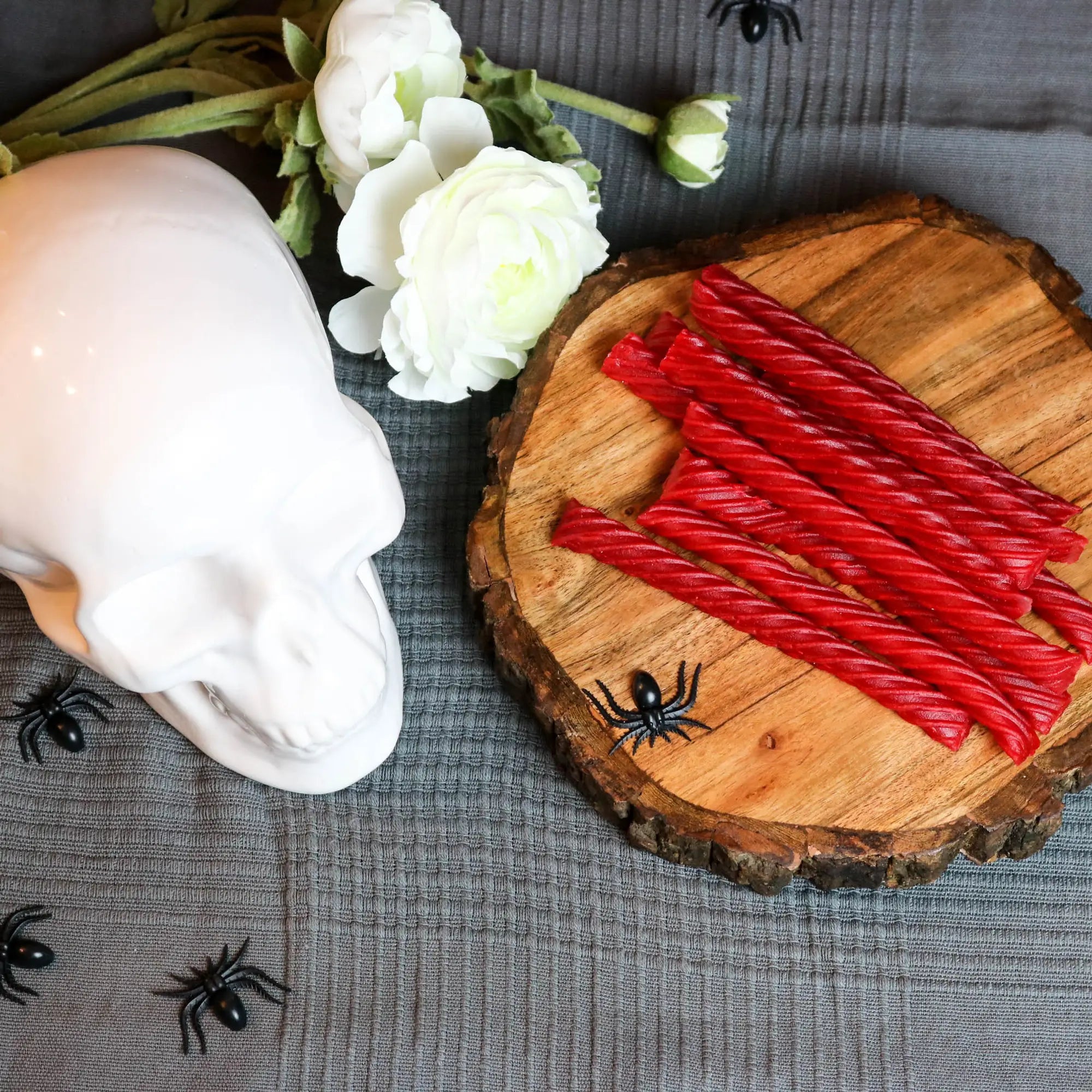 Red Vines Original Red Jumbo Licorice Twists in a spooky Halloween scene with fake spiders, a white skull and white roses