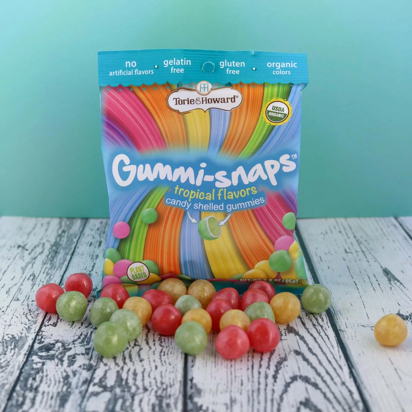 Cylindrical shaped red, yellow, and green candy in front of a Torie & Howard Gummi-Snaps Tropical Flavors Bag