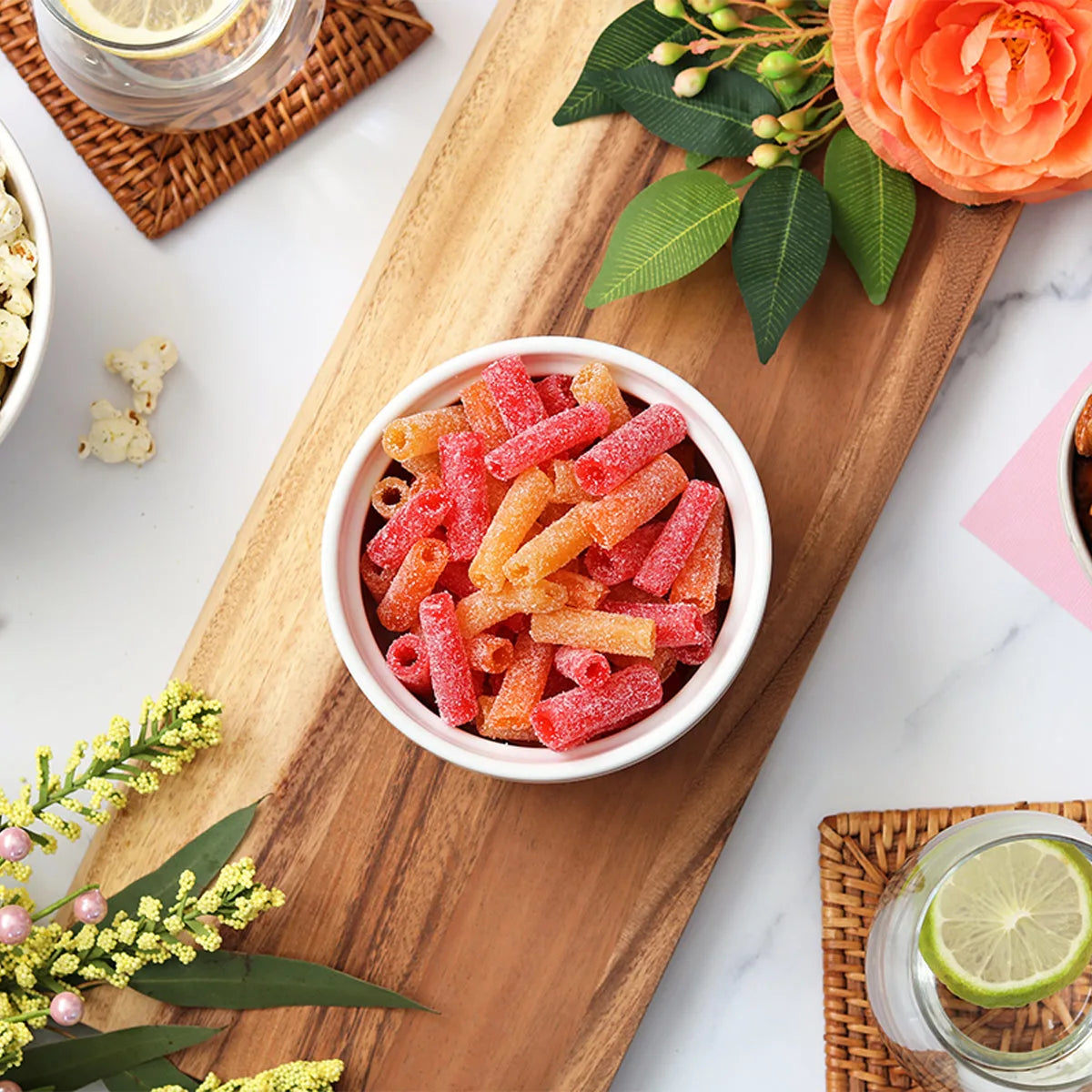 Sour Punch Tropical Bites candy in a dish surrounded by spring flowers and other snacks