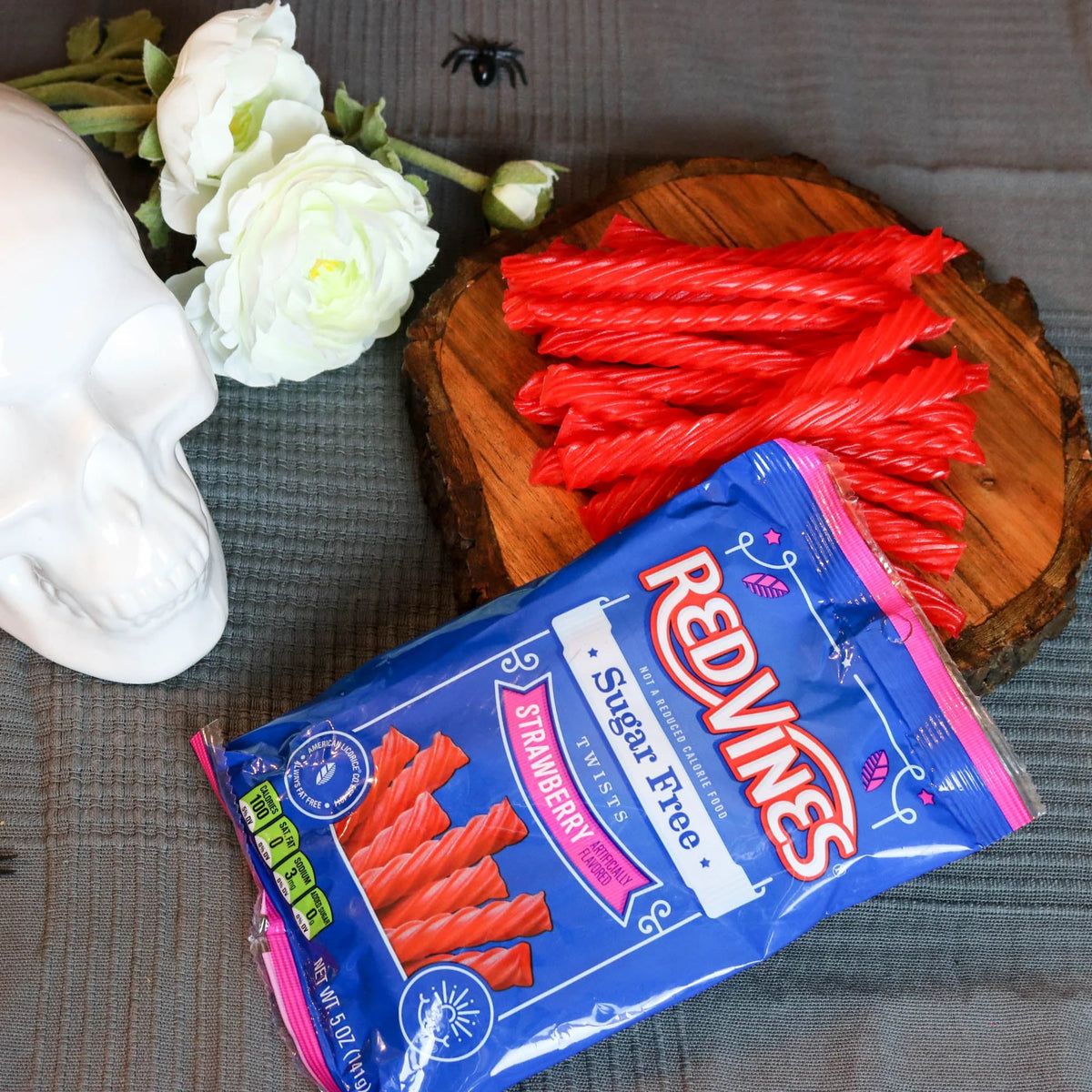 Red Vines Strawberry Sugar Free Licorice in a spooky Halloween scene with fake spiders, a white skull and white roses