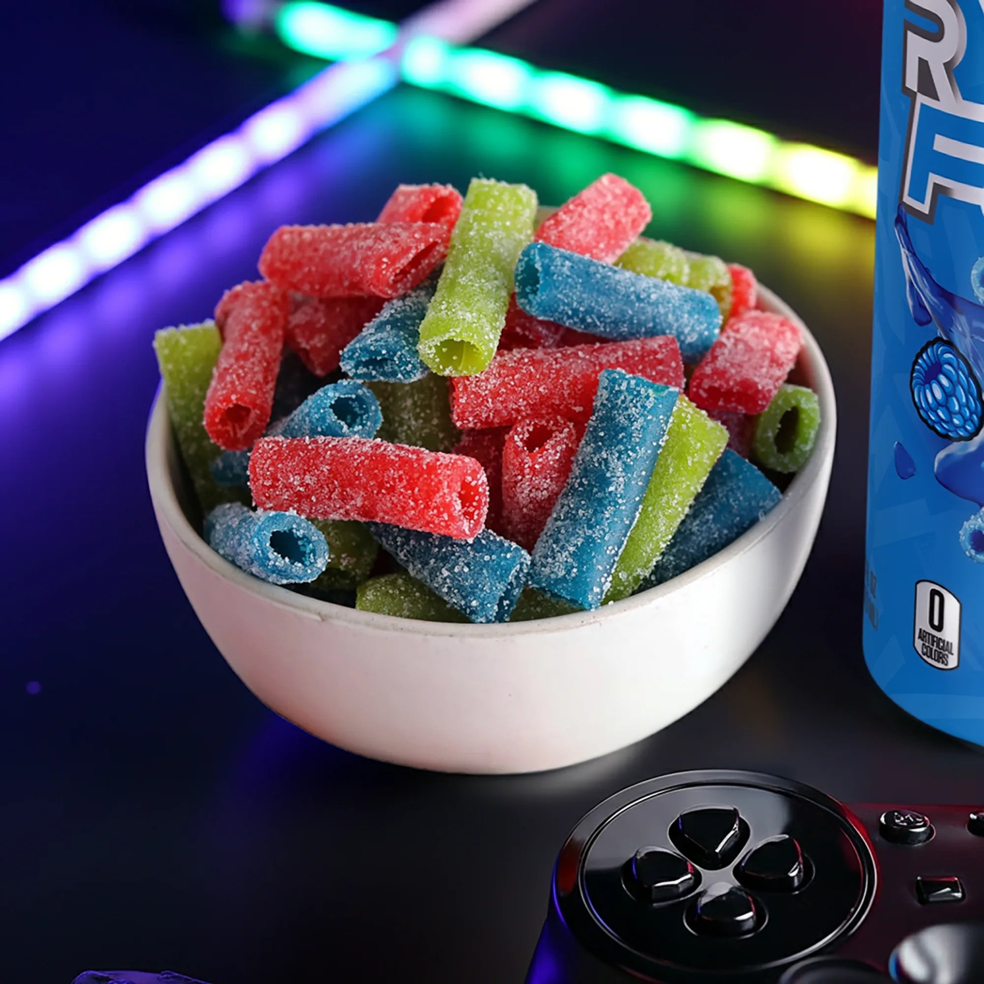 Bowl of assorted sour candy bites next to an energy drink and video game controller 