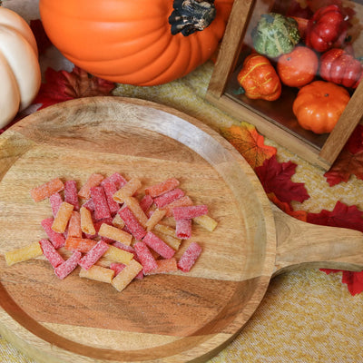 Sour Punch Tropical Bites Candy on a round wooden plate surrounded by pumpkins and leaves