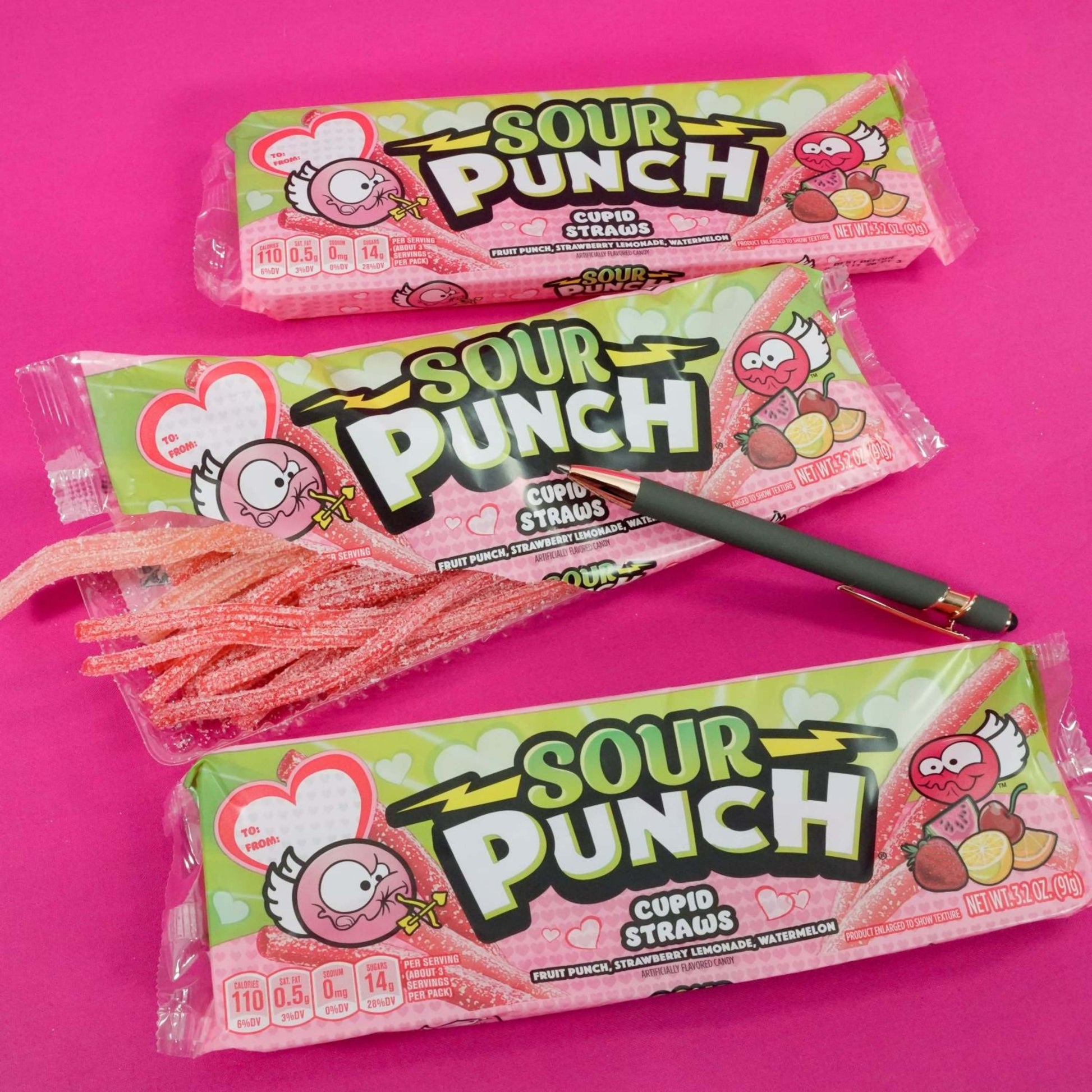 SOUR PUNCH Cupid Straws valentine candy trays on pink tablecloth with a pen