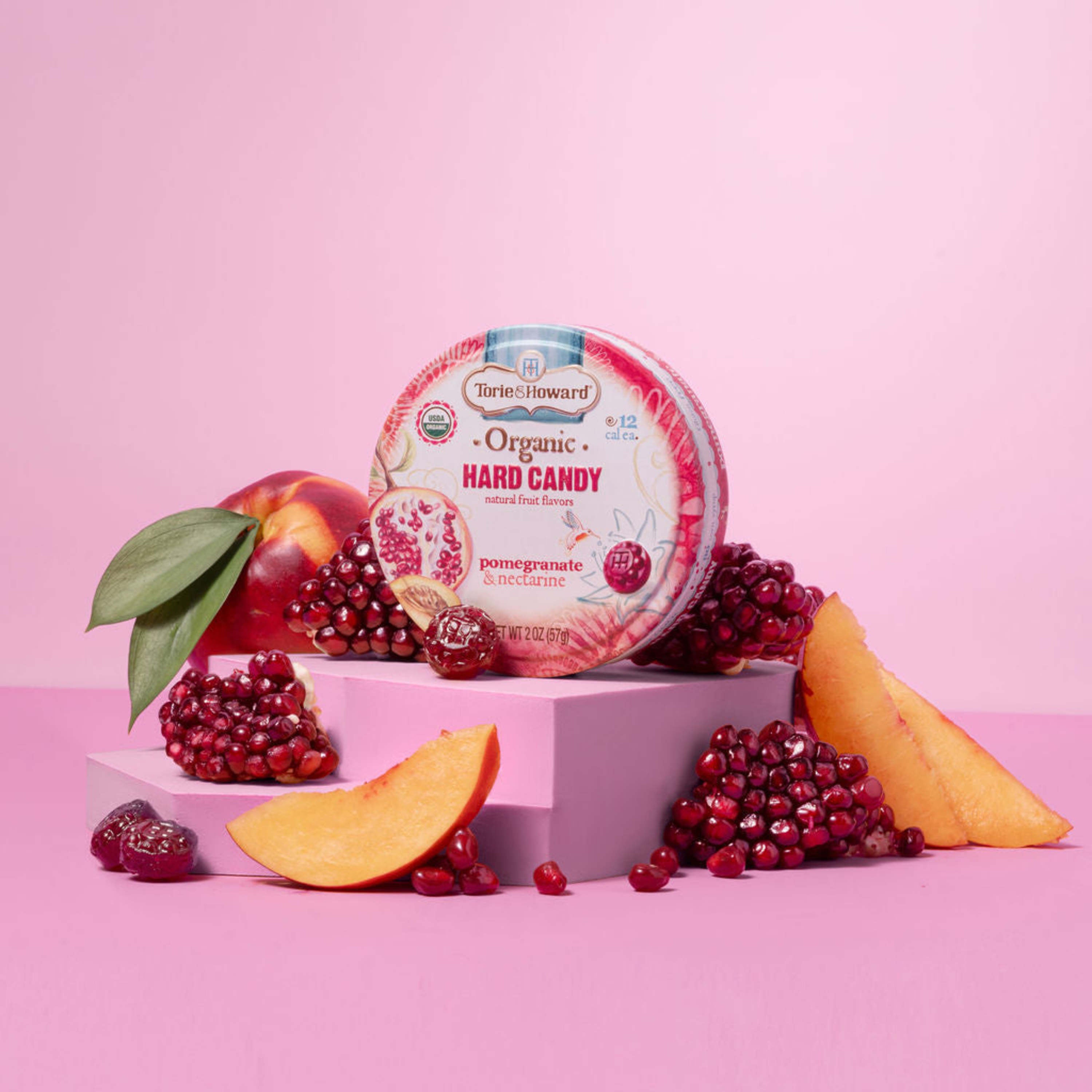 Torie & Howard Pomegranate & Nectarine Organic Hard Candy 2oz Tin surrounded by fresh fruit and candy pieces