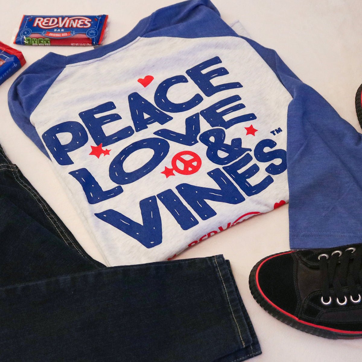 RED VINES Peace, Love & Vines T-Shirt with blue jeans, black sneakers, and some Red Vines Licorice