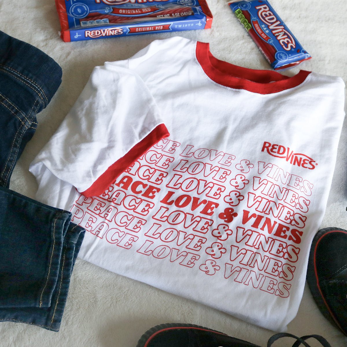 RED VINES Red and White Peace, Love & Vines T-Shirt with blue jeans, black sneakers, and Red Vines Licorice