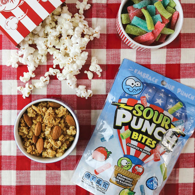 Sour Punch Assorted Americana Summer Candy Bites on a picnic blanket with popcorn and other summer snacks