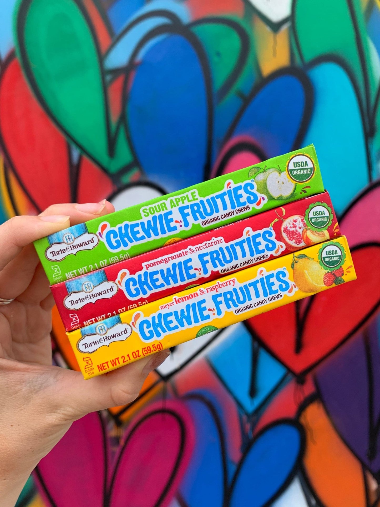 Torie & Howard Chewie Fruities Sour Apple, Pomegranate & Nectarine, and Meyer Lemon & Raspberry Stick Packs with heart graffiti background